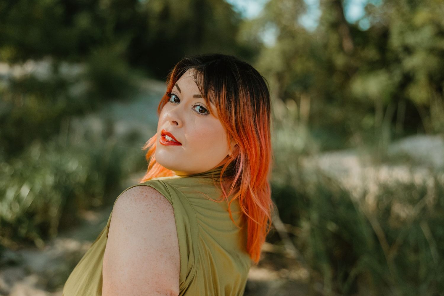Woman with vibrant red-orange hair in olive dress posing outdoors in natural sunlight. Photographer branding session at the Indiana Dunes.