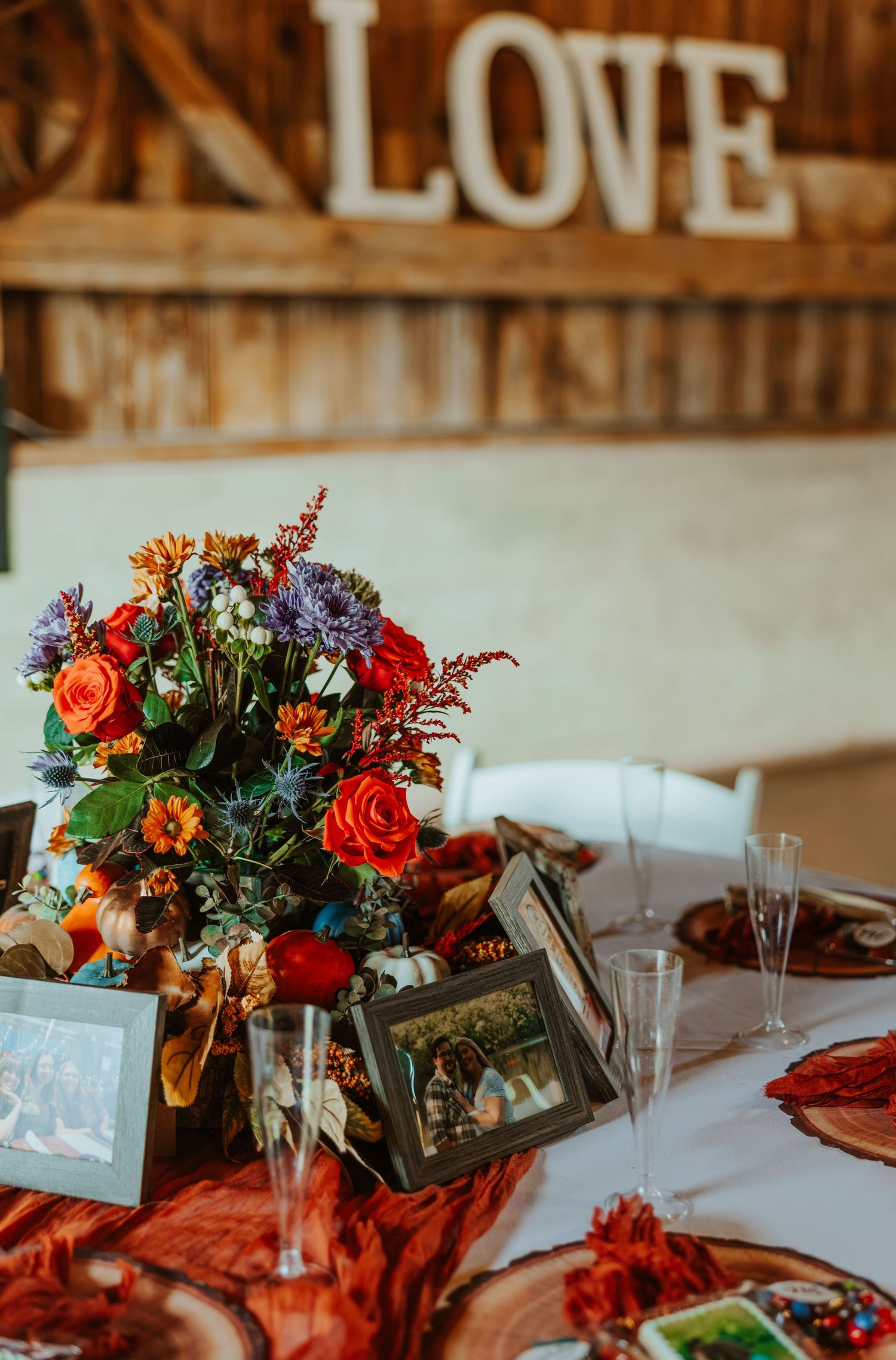 Colorful fall wedding centerpiece with roses beside framed photos under a LOVE sign.