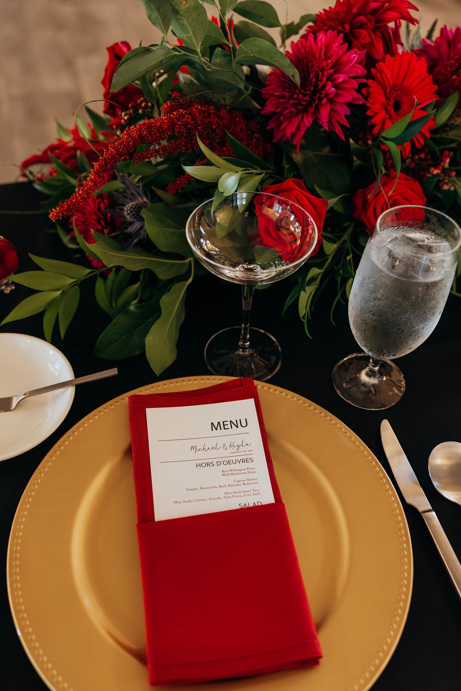 Elegant wedding table setting with gold charger plate, red napkin, menu card, and red floral centerpiece. Crown Point Courthouse wedding.