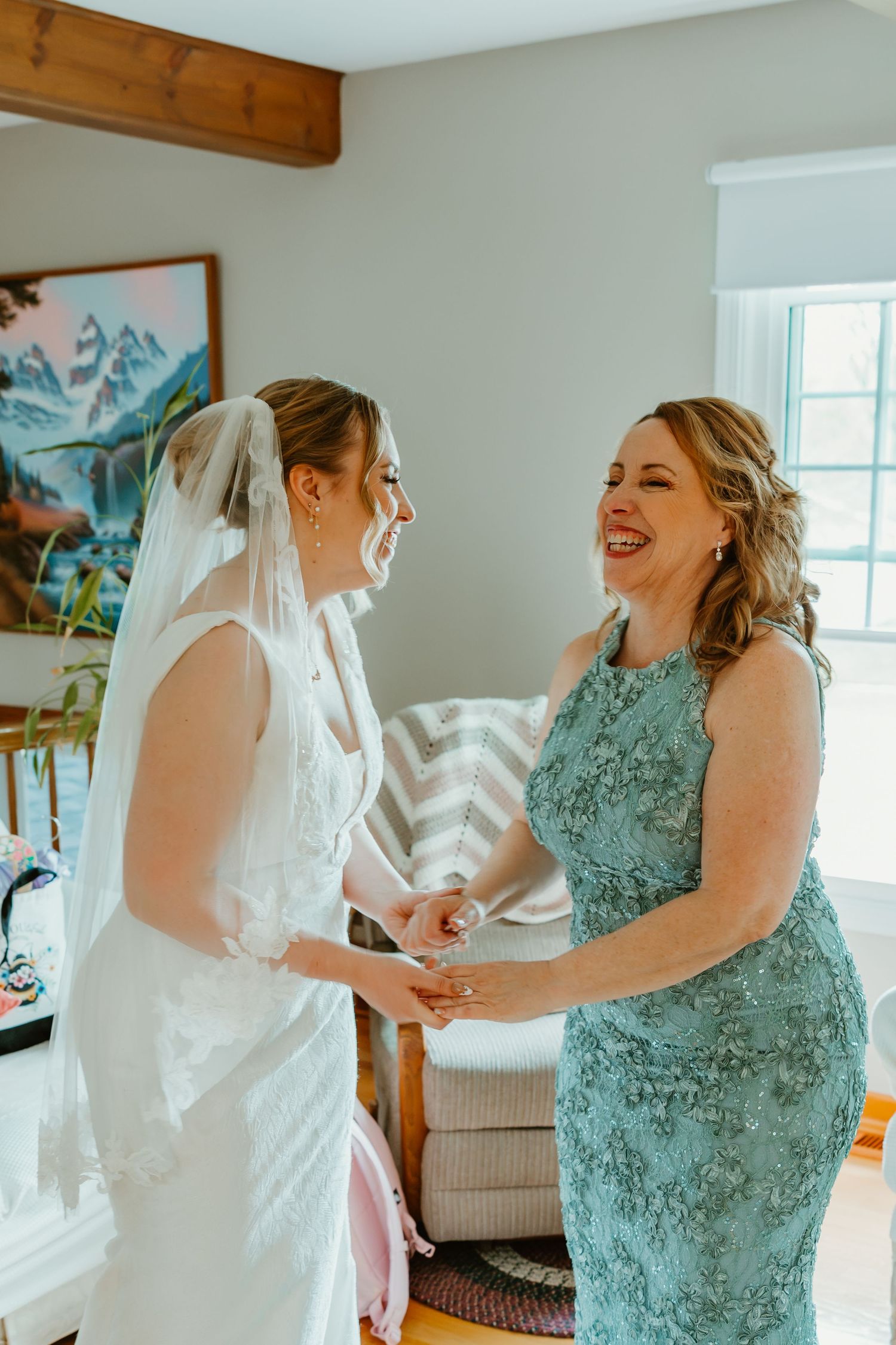 Joyful bride in white wedding gown and veil laughing with her mother in a teal lace dress. Chicago documentary style photography.