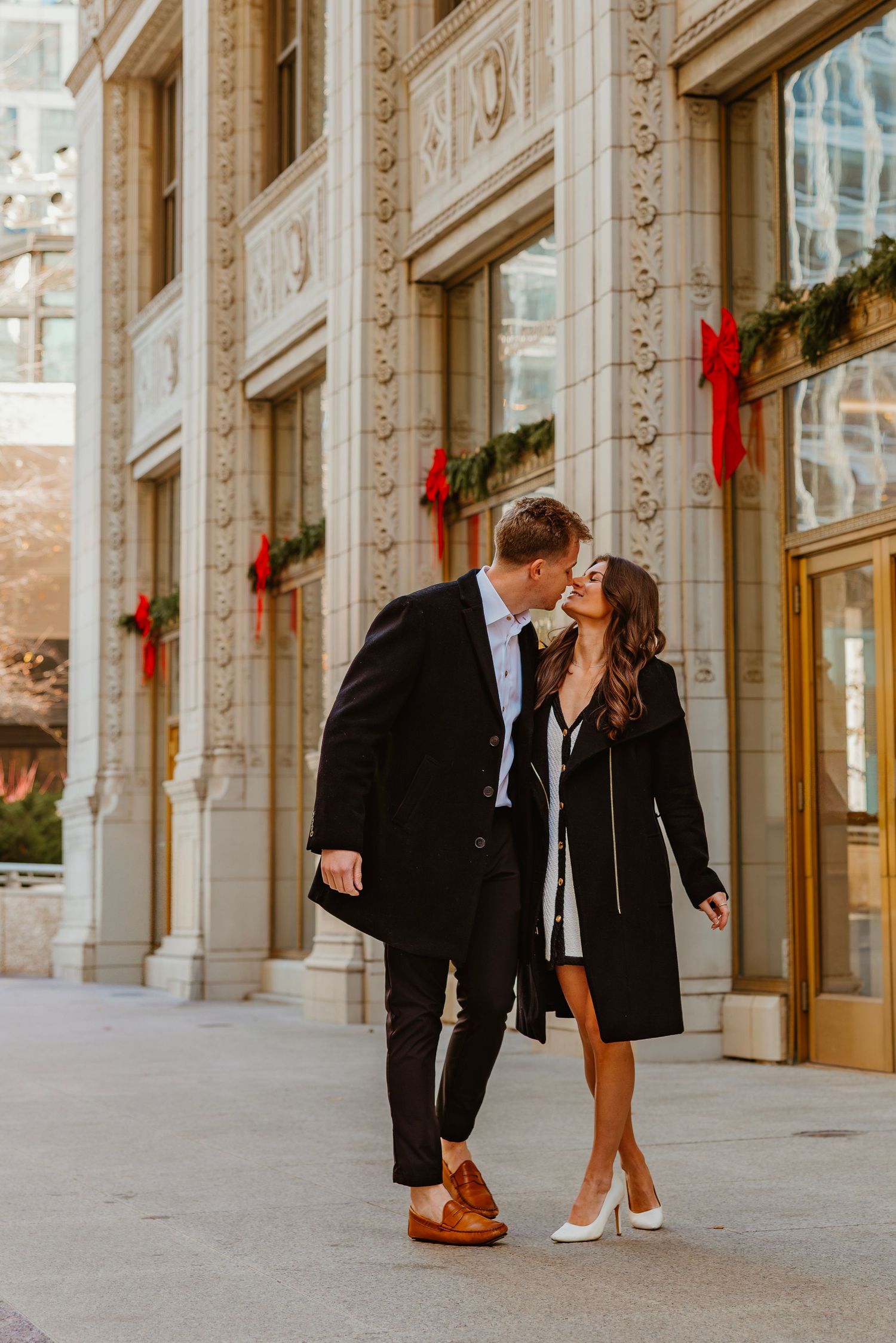 Couple sharing a kiss outside an ornate building decorated with festive red holiday wreaths. Outdoor Chicago engagement photos.