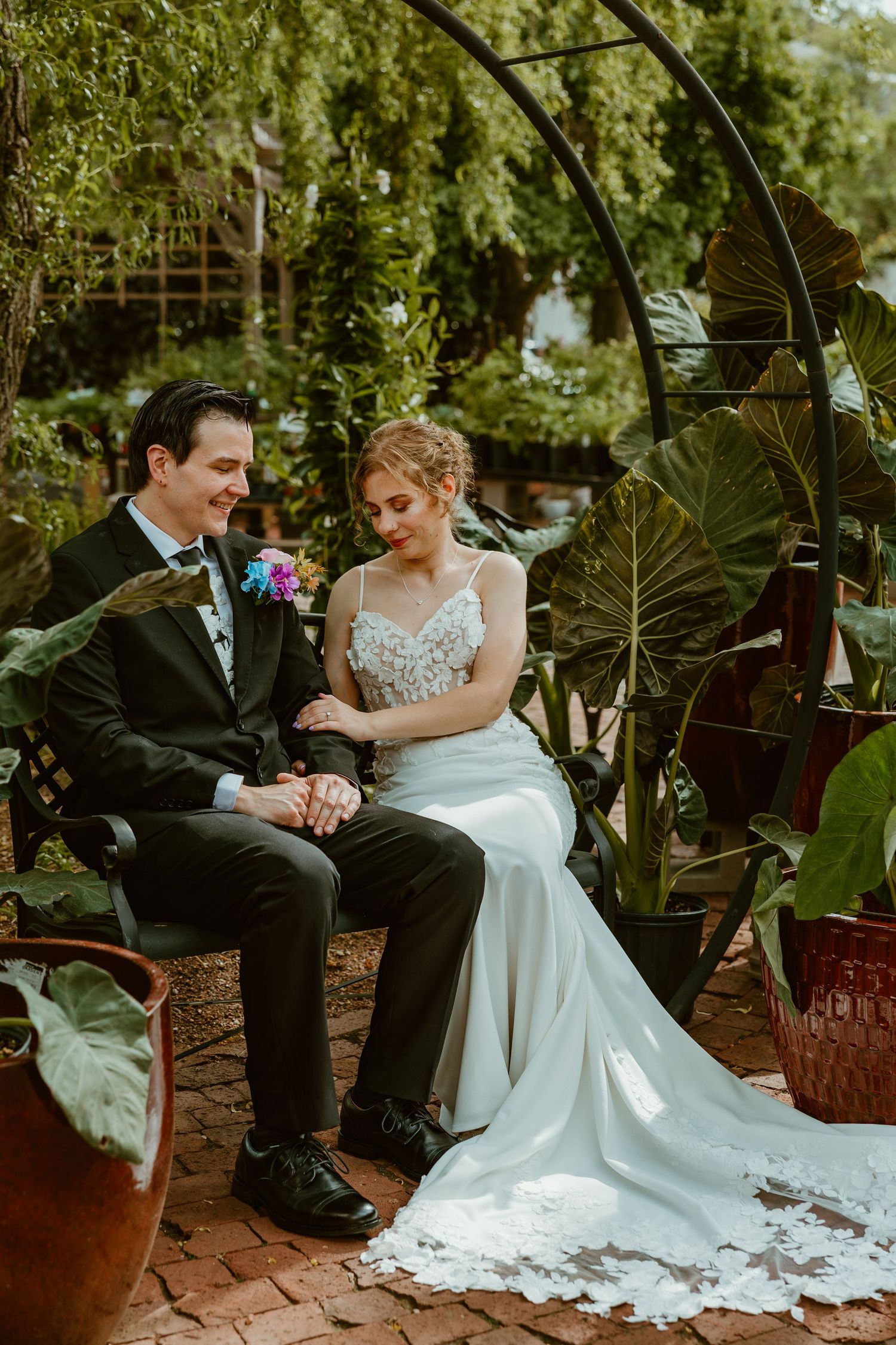 Bride and groom sitting together on a garden bench under a metal arch surrounded by lush tropical plants. Chicagoland wedding venues.