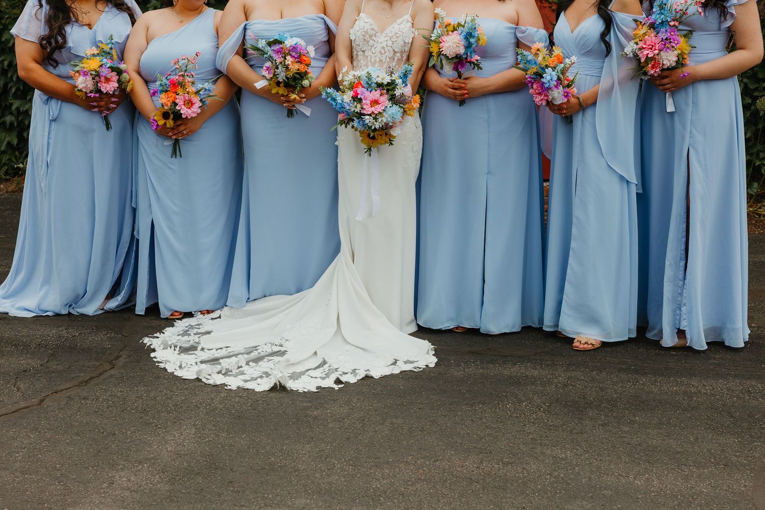 Bride and bridesmaids in light blue gowns displaying colorful bouquets at outdoor wedding. Chicagoland wedding venues.