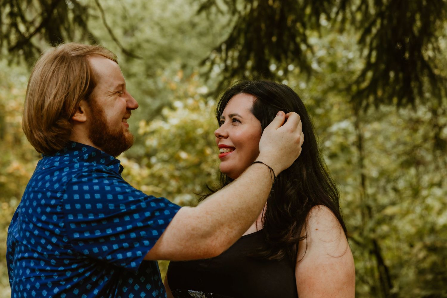 Romantic couple sharing a tender moment outdoors surrounded by lush green trees in natural setting. Northwest Indiana wedding engagement.