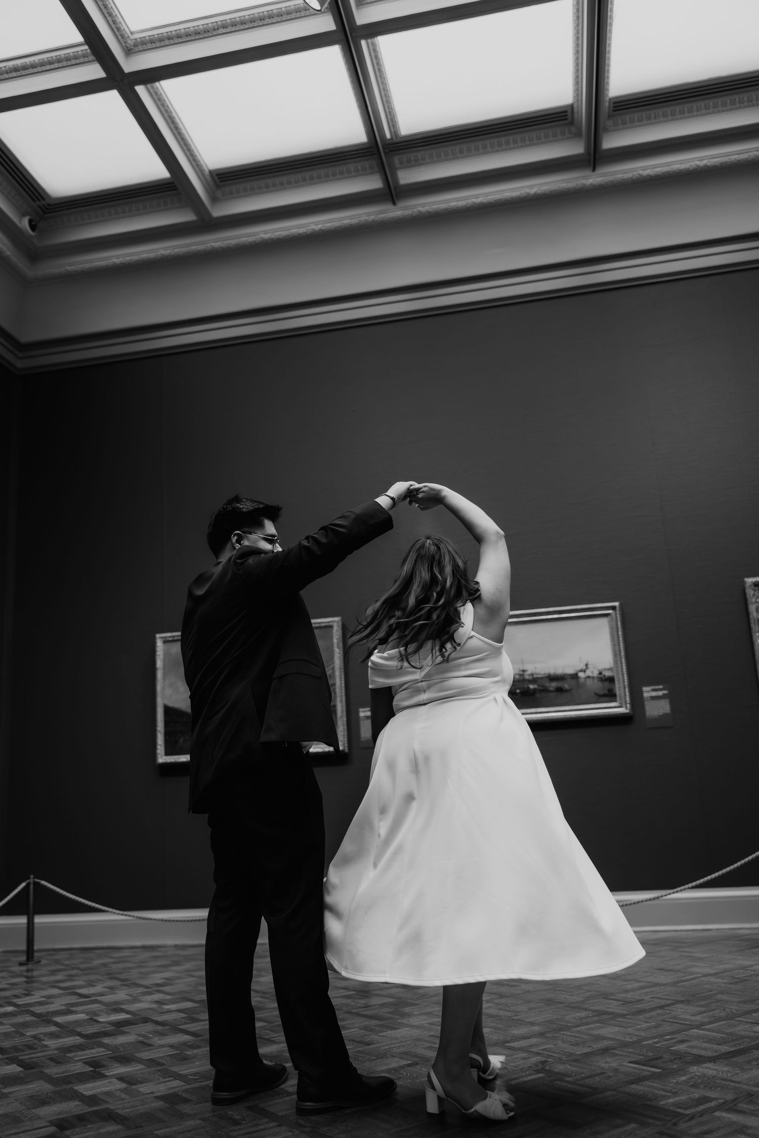 Black and white photo of couple dancing in elegant art museum gallery. Art Institute engagement photos.
