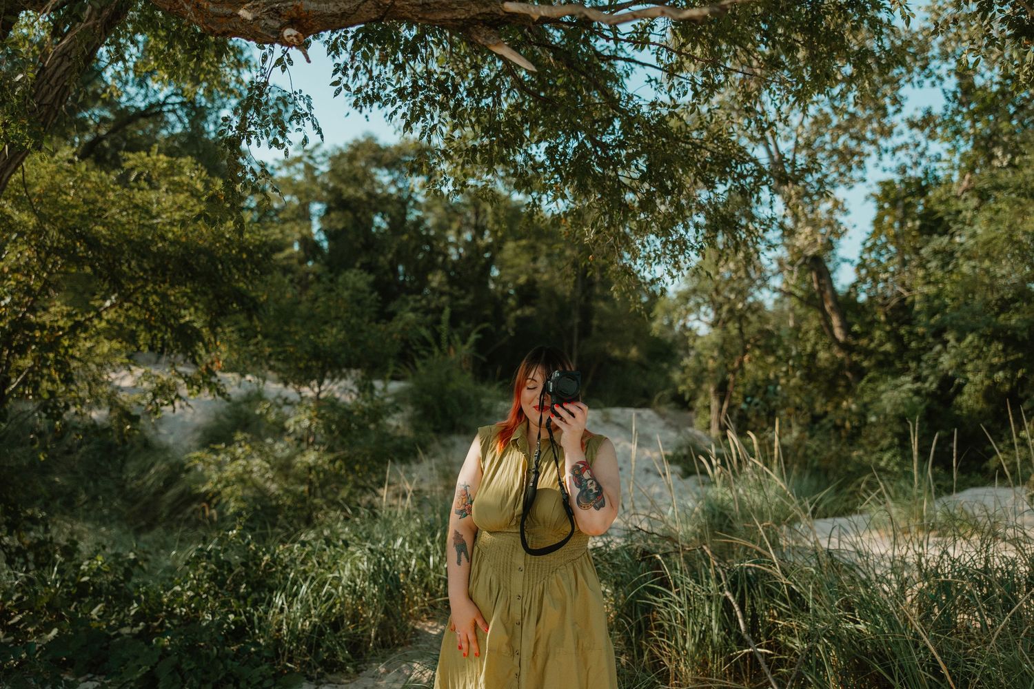 Woman in olive maxi dress photographing nature in a lush green outdoor setting. Photographer branding session at the Indiana Dunes.
