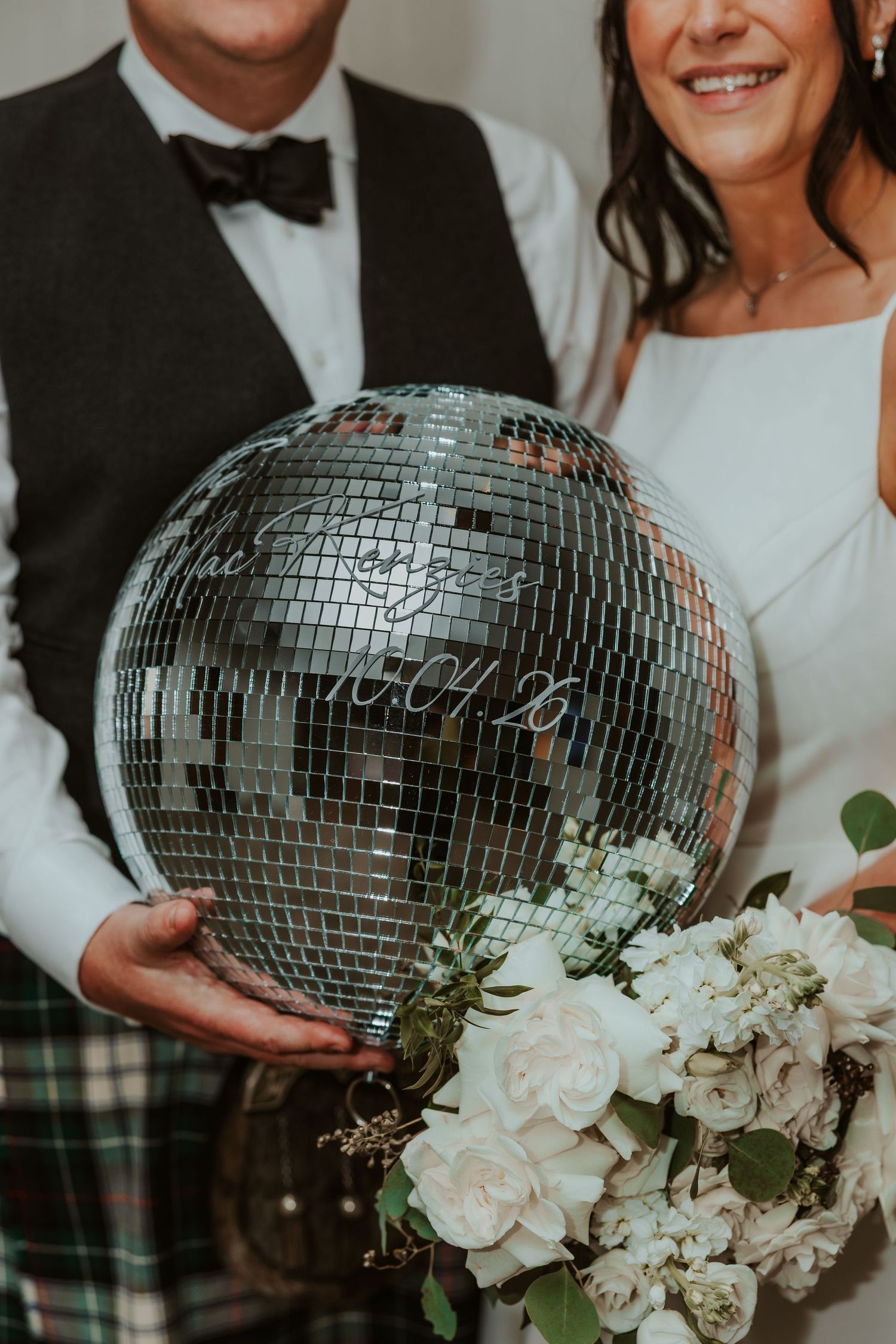 Bride and groom holding a personalized mirrored disco ball with wedding date, alongside a white floral bouquet. Chicago Thompson Hotel