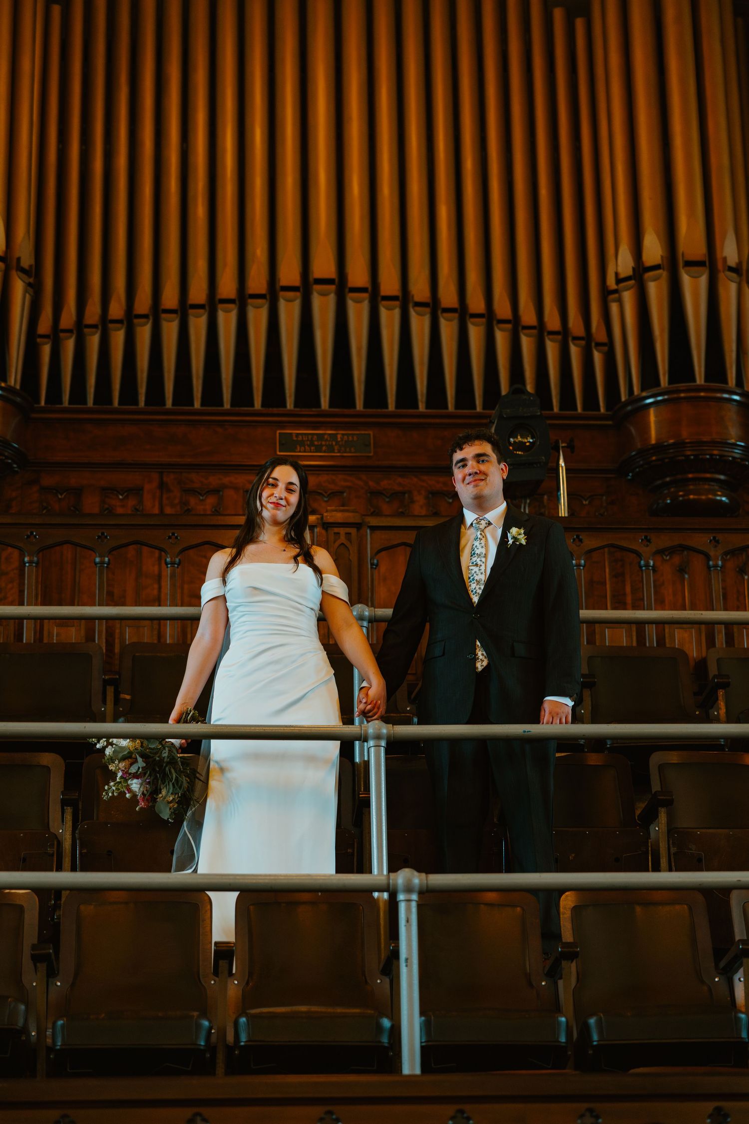 Wedding couple holding hands in front of a grand pipe organ in a historic church balcony.