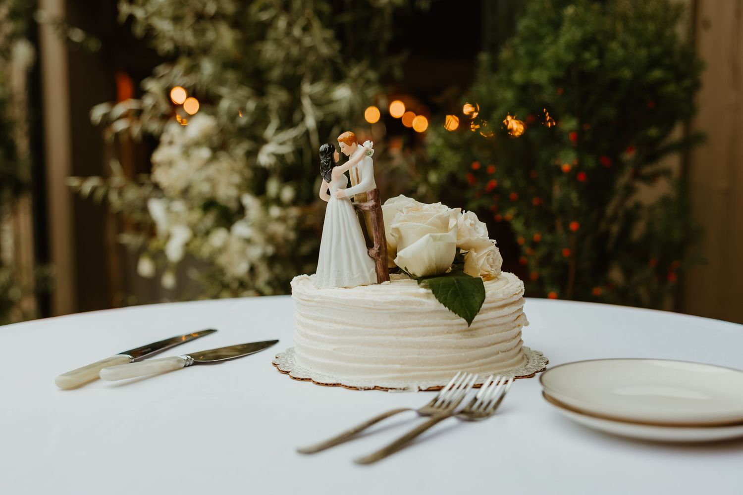 White wedding cake with bride and groom topper and white roses on table with cake cutting utensils. Northwest Indiana wedding venues.