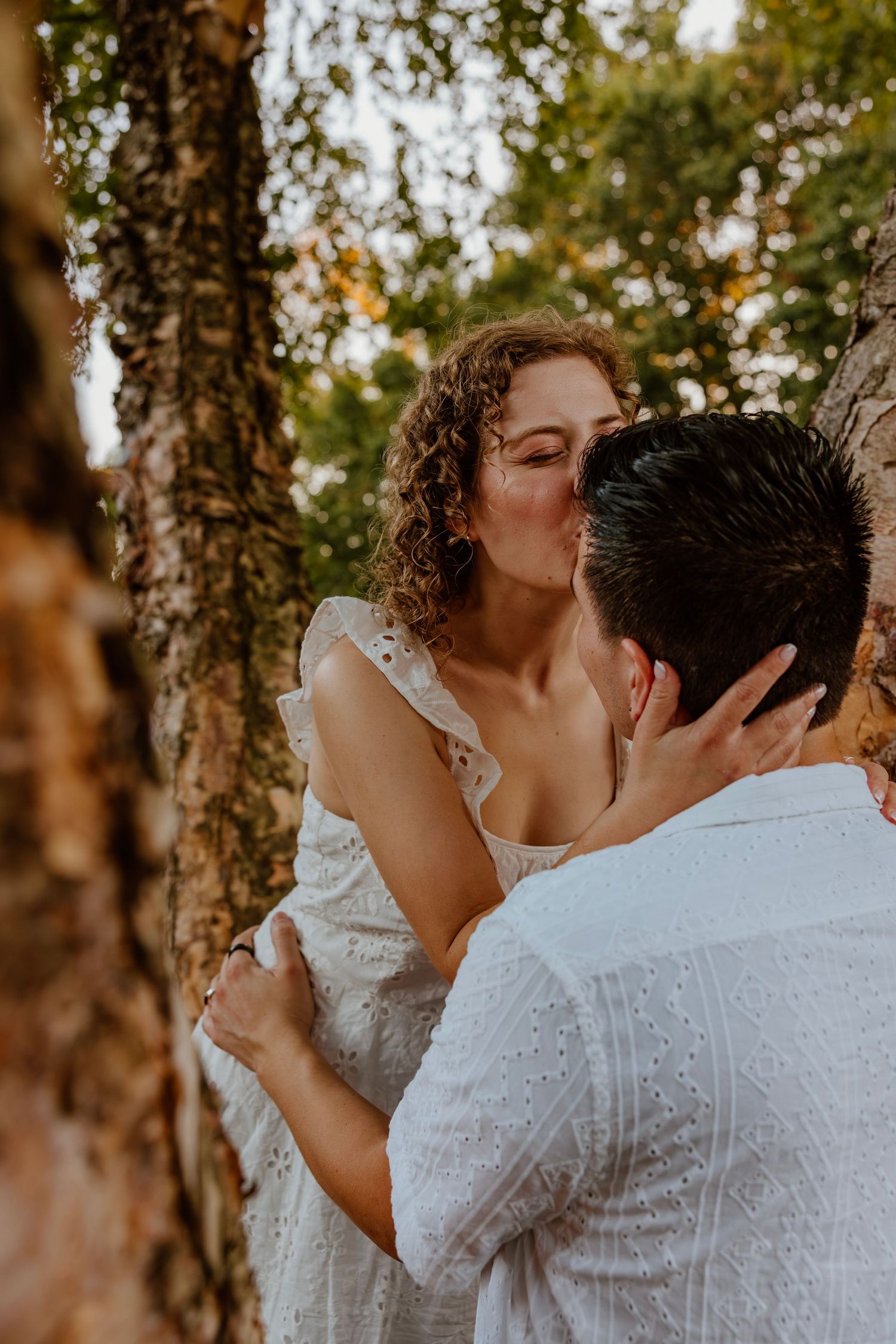 Bride with curly hair kissing groom among birch trees in romantic outdoor wedding portrait. Chicagoland engagement photos.