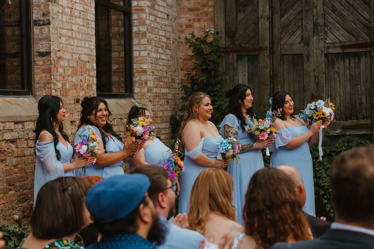 Bridesmaids in light blue off-shoulder gowns holding colorful wildflower bouquets at outdoor brick venue wedding. Chicagoland wedding venues
