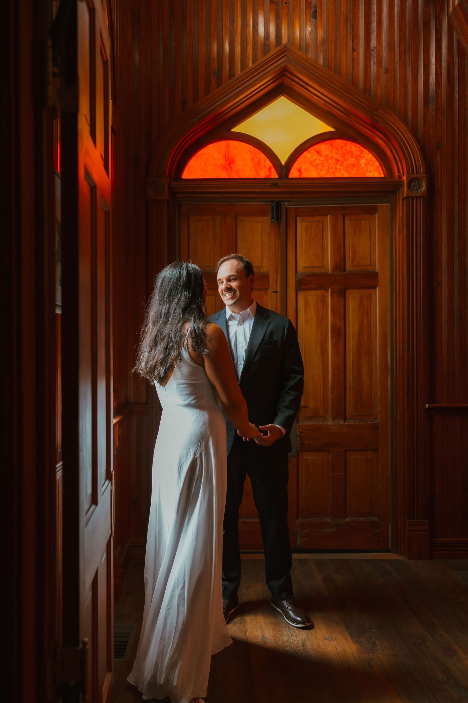 Bride and groom share a tender first look moment by ornate wooden doors with warm stained glass. Michigan elopement.
