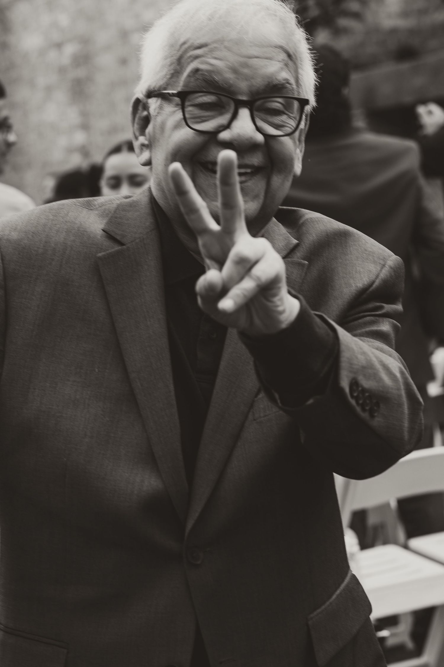 A smiling elderly man in a suit and glasses flashes a peace sign at a wedding ceremony. Chicagoland wedding venues.