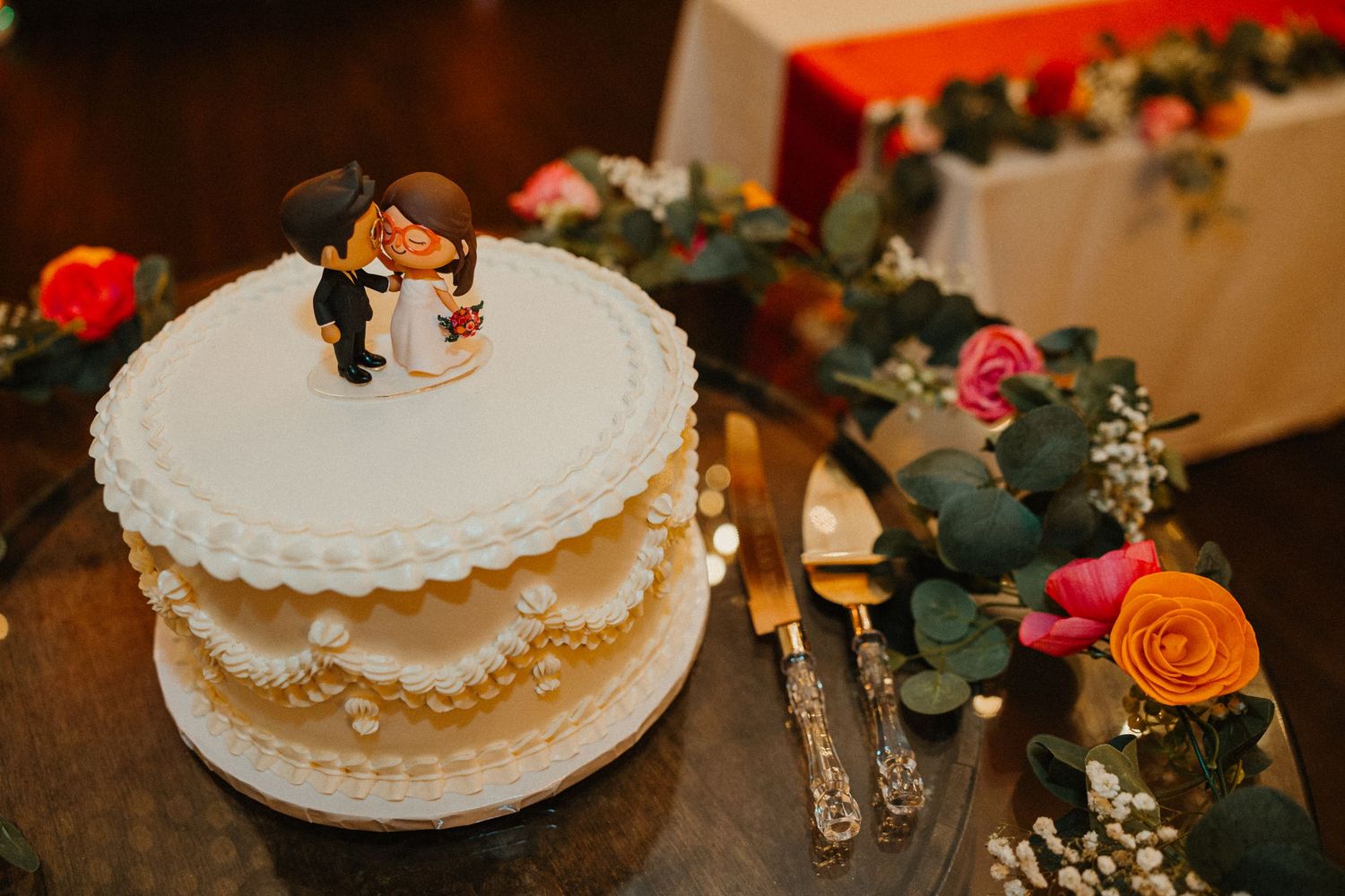 Two-tier white wedding cake with bride and groom figurine topper on rustic barrel with floral greenery. Chicagoland wedding venues.