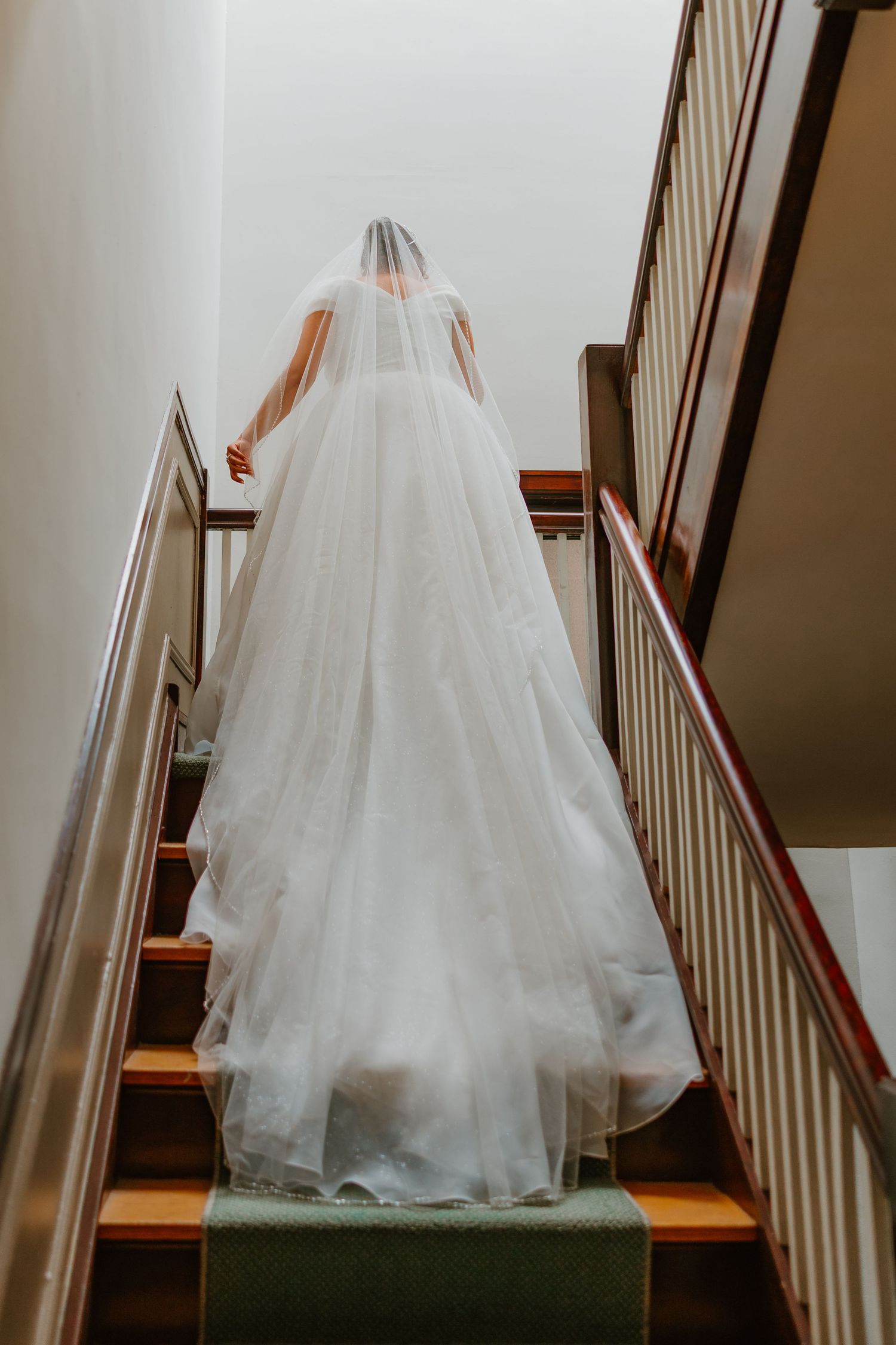 Elegant bride ascends staircase in flowing white ball gown with long cathedral veil trailing behind her. Chicagoland weddings.