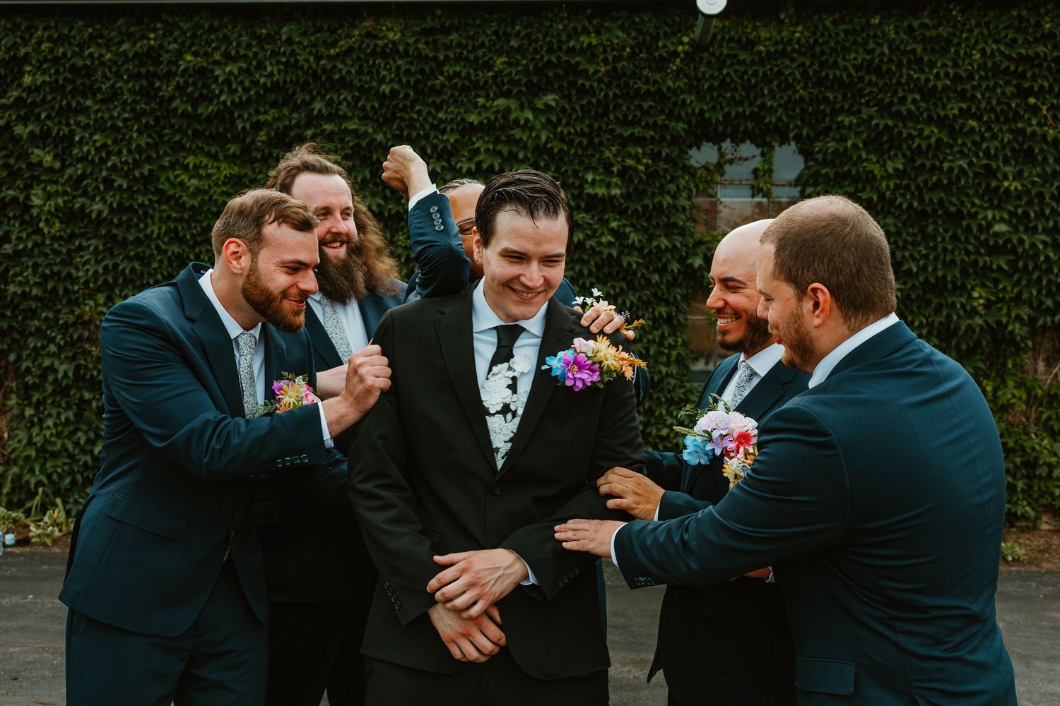 Groom and groomsmen in navy suits with colorful boutonnieres laughing together outside. Chicagoland wedding venues.