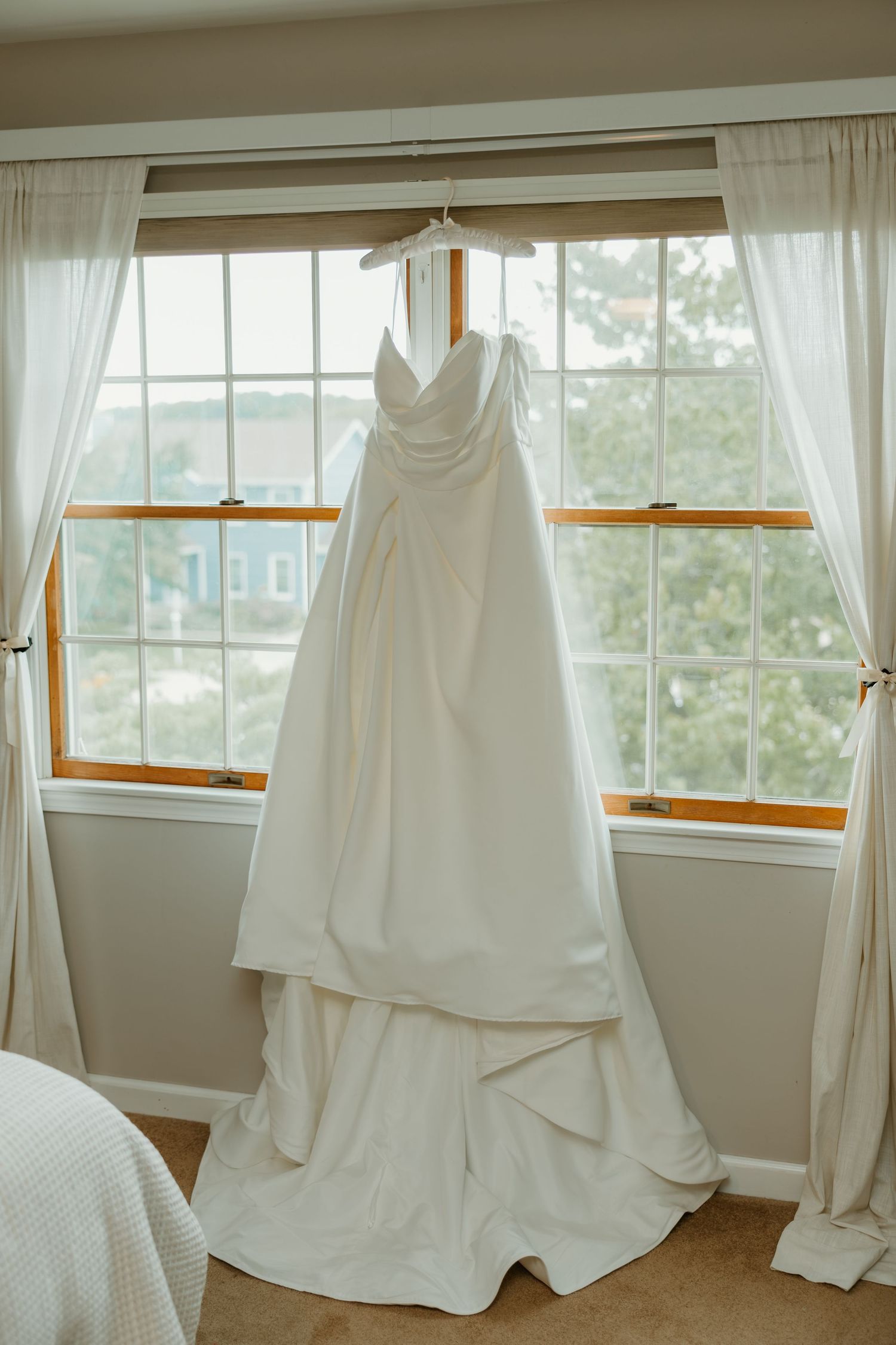 Classic white strapless wedding gown with layered skirt hanging in window before bridal ceremony. Northwest Indiana wedding venues.