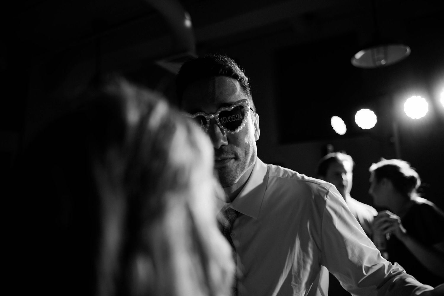 Man wearing sunglasses dancing at a wedding reception in black and white.