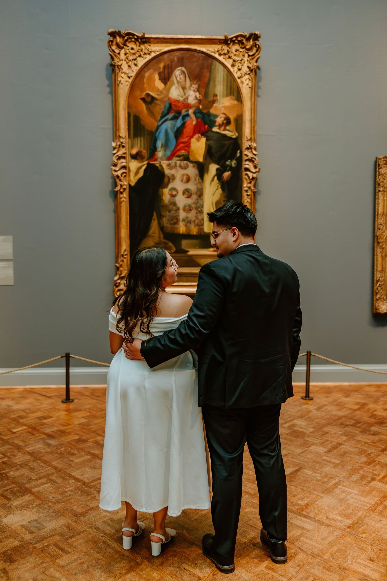 Couple in wedding attire viewing ornate religious painting in art museum gallery together. Art Institute of Chicago engagement photos.