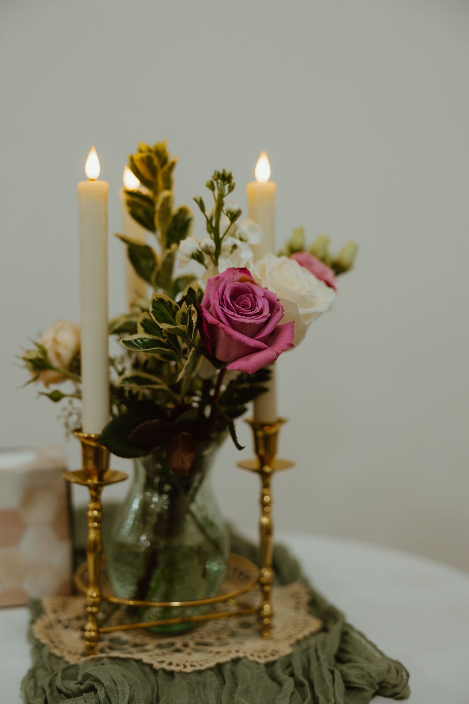 Elegant wedding centerpiece with lit white candles in gold holders and pink roses in a glass vase.