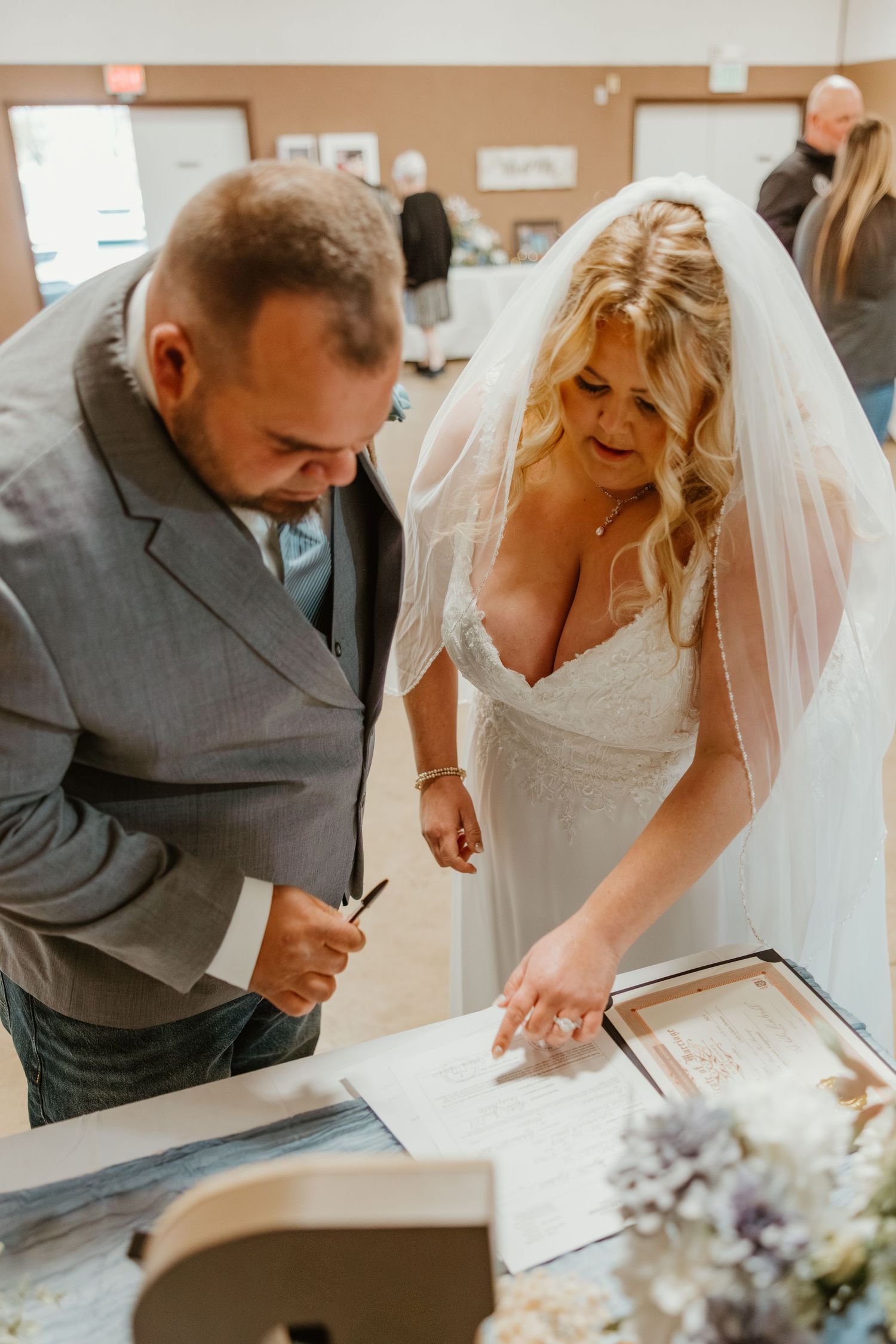 Bride in white gown and veil signs wedding documents alongside groom in grey suit. Northwest Indiana wedding venues.