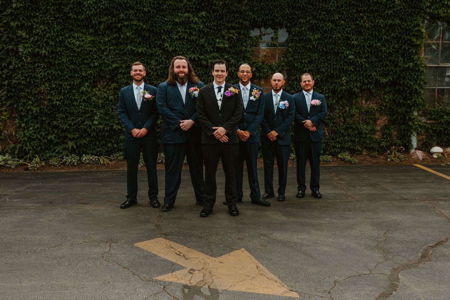 Groomsmen in navy suits standing together on pavement in front of ivy-covered wall. Chicagoland wedding venues.
