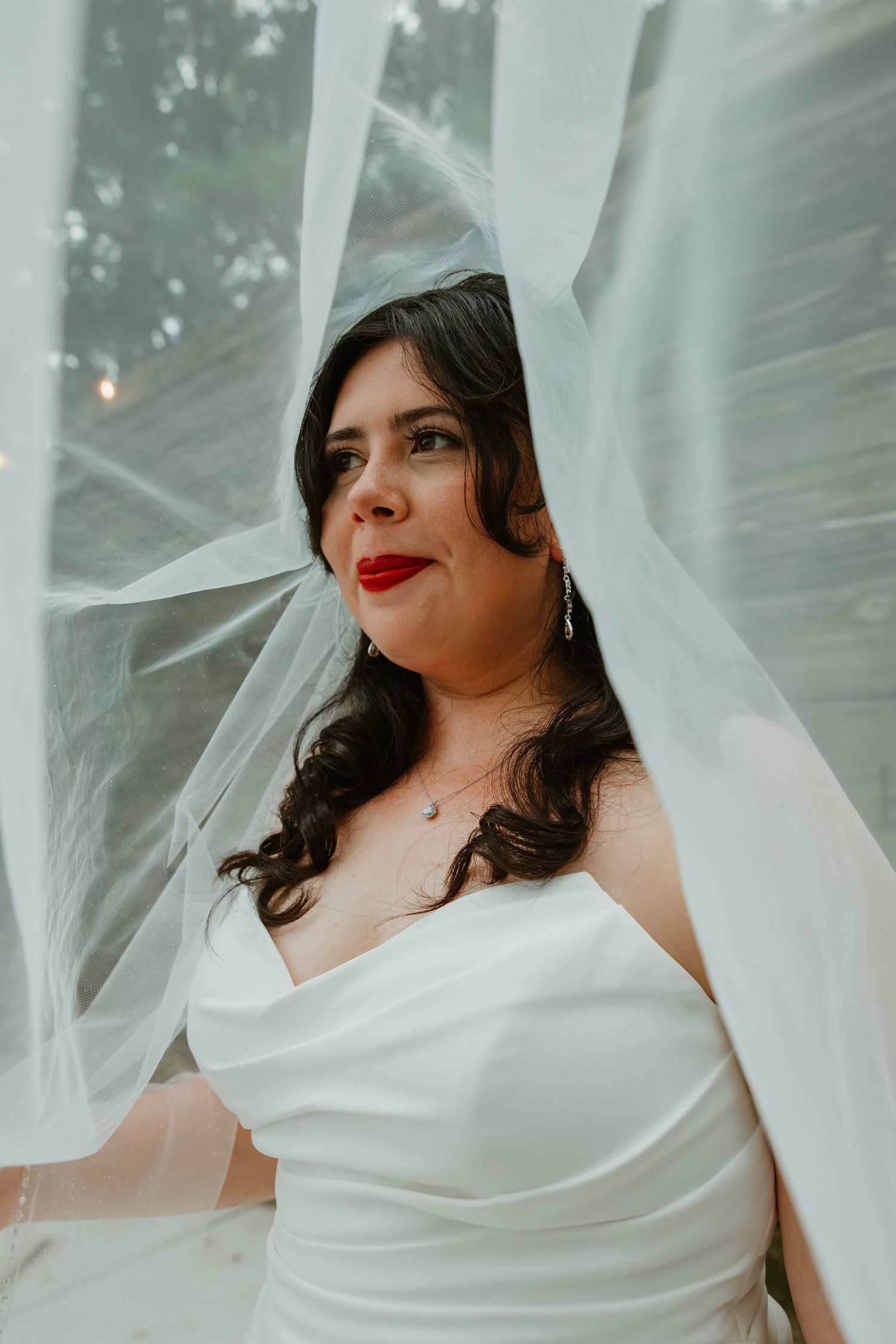 Beautiful bride with red lips and dark curls poses gracefully beneath her flowing white veil at a wedding. Northwest Indiana wedding venues.