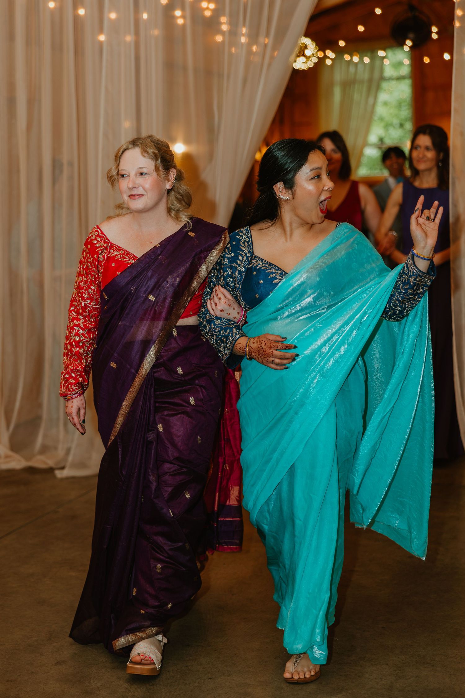 Two women in colorful saris walk together at Indian wedding reception celebration. Documentary style wedding photos.