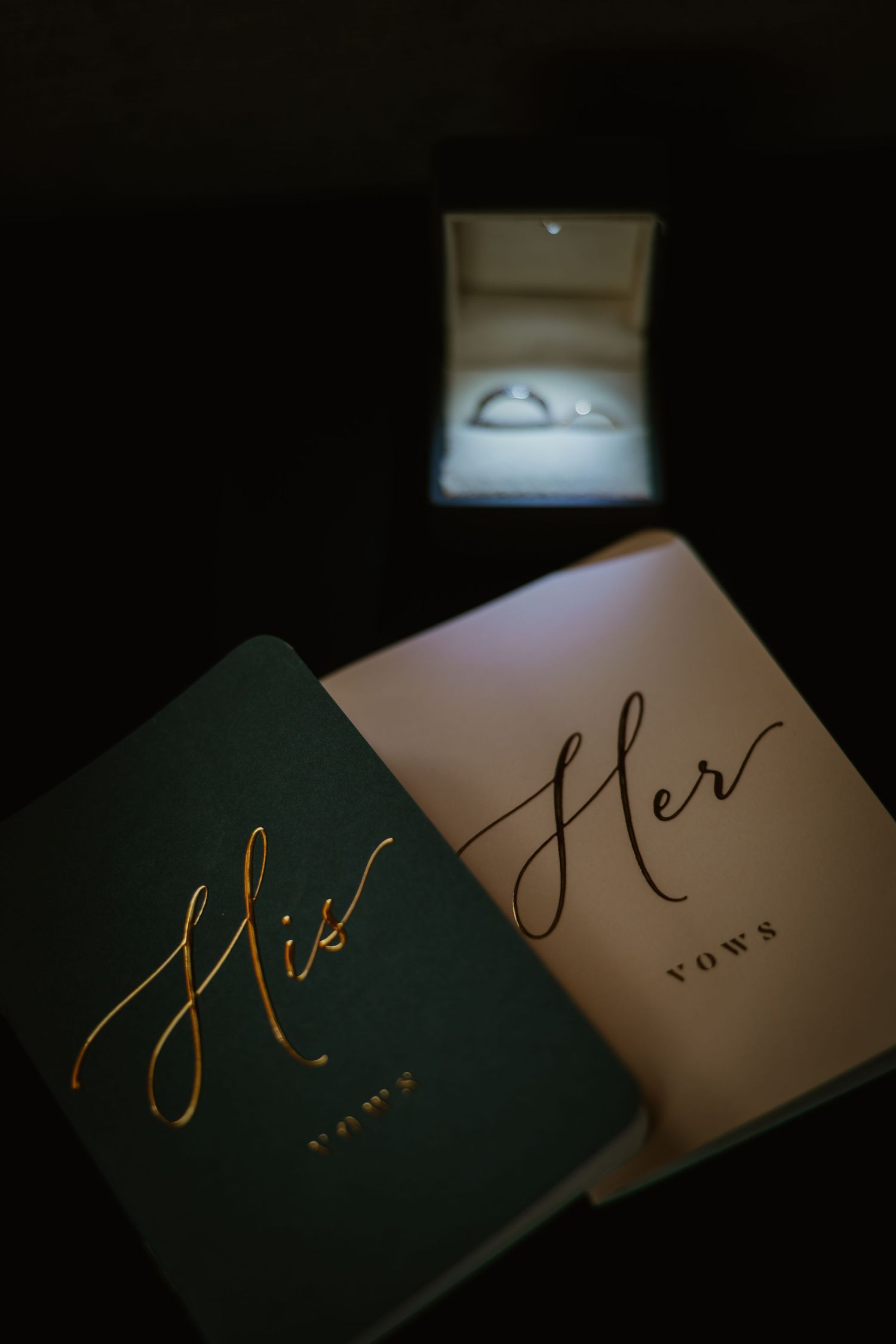 His and Her vow books displayed with glowing wedding ring box in background. Documentary style wedding photos.