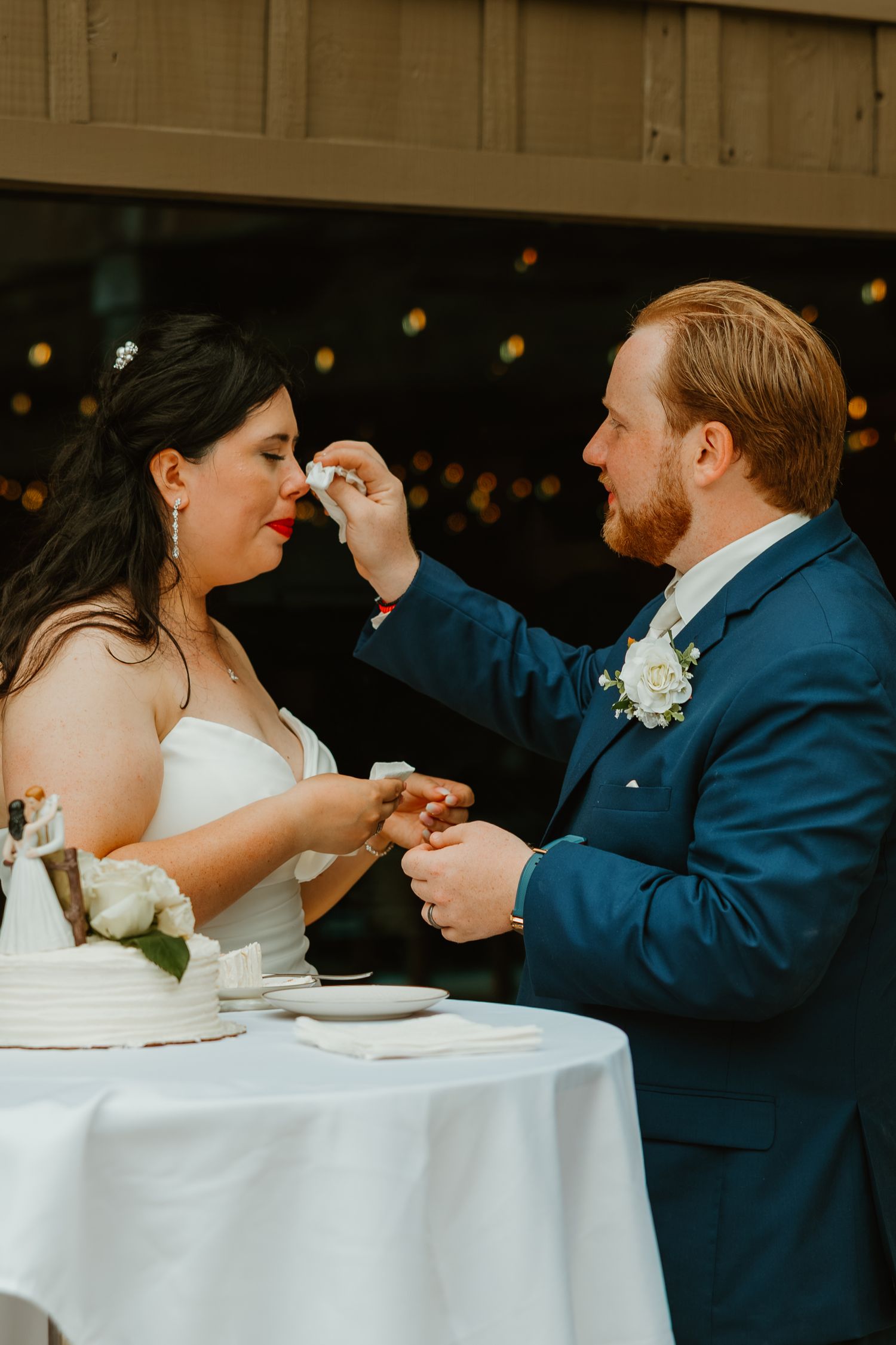 Groom tenderly wiping frosting from brides face during wedding cake cutting at outdoor reception. Northwest Indiana wedding venues.