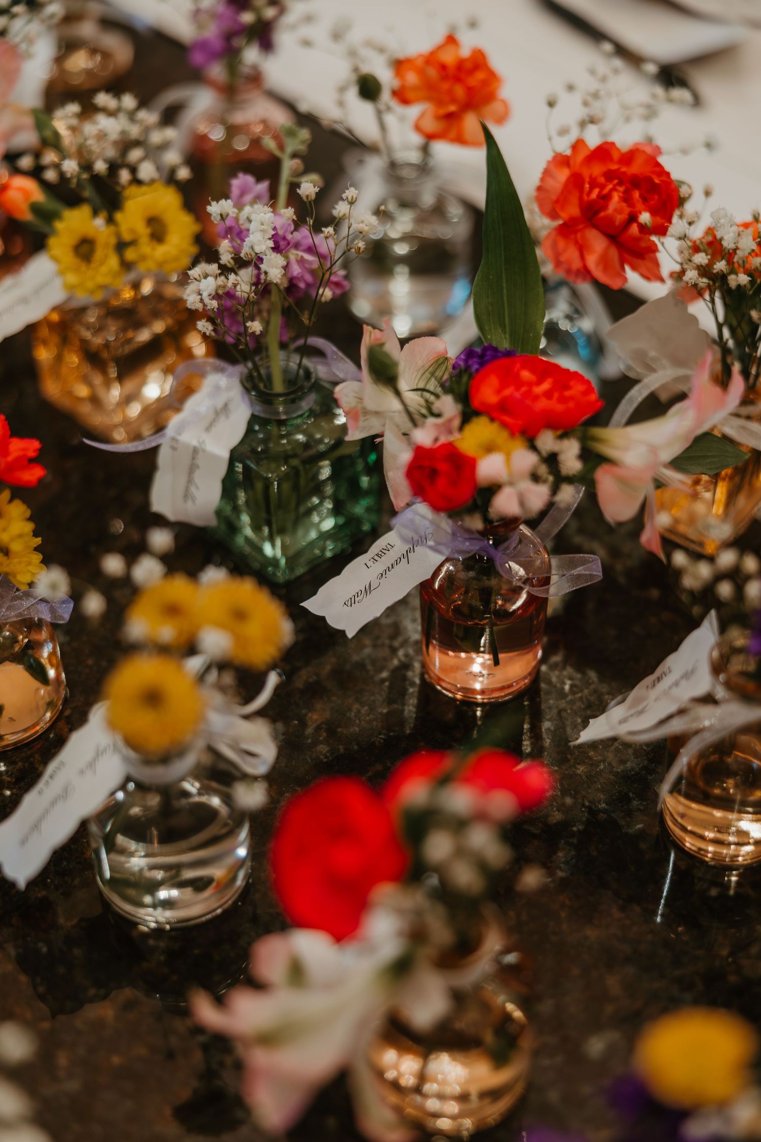 Vibrant wedding reception centerpiece featuring colorful flowers in vintage glass bottles with place cards. Chicagoland wedding venues.