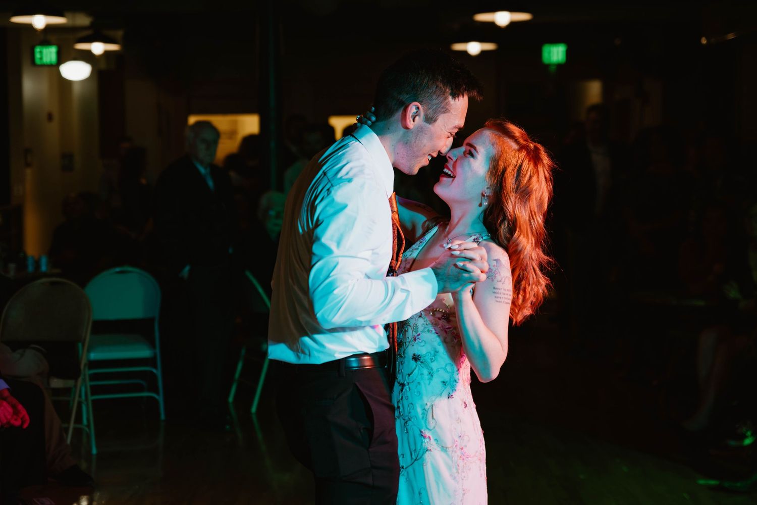 Bride and groom sharing an intimate first dance under colorful reception lighting.