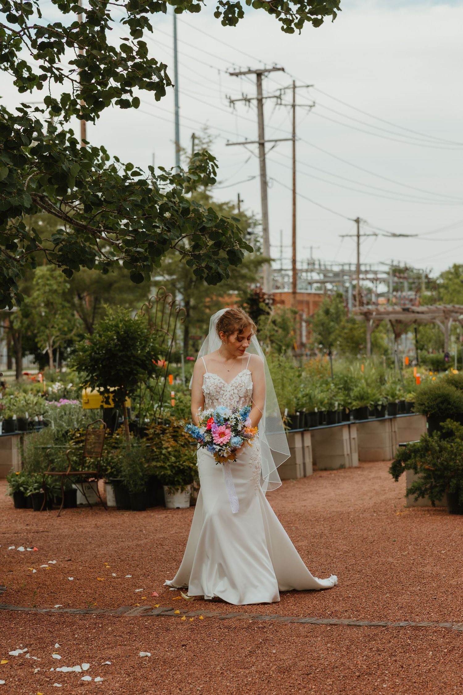 Bride in fitted lace wedding gown holding colorful bouquet walking through garden nursery with veil flowing. Chicagoland wedding venues.