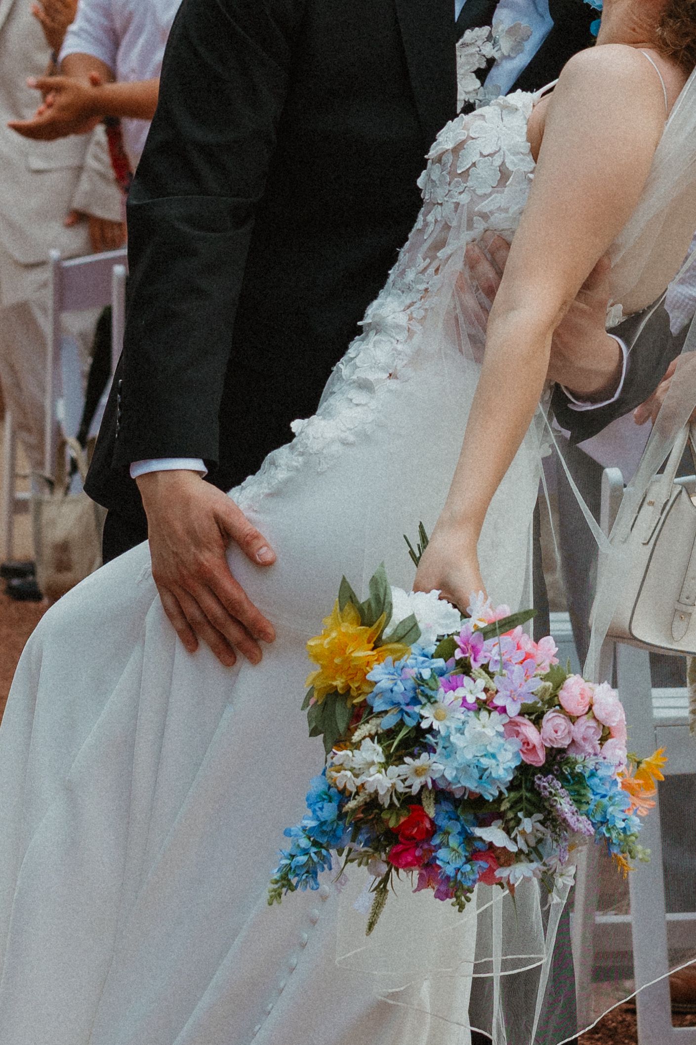 Bride holding colorful wildflower bouquet in white lace gown beside groom in black suit at outdoor wedding ceremony. Chicagoland wedding.