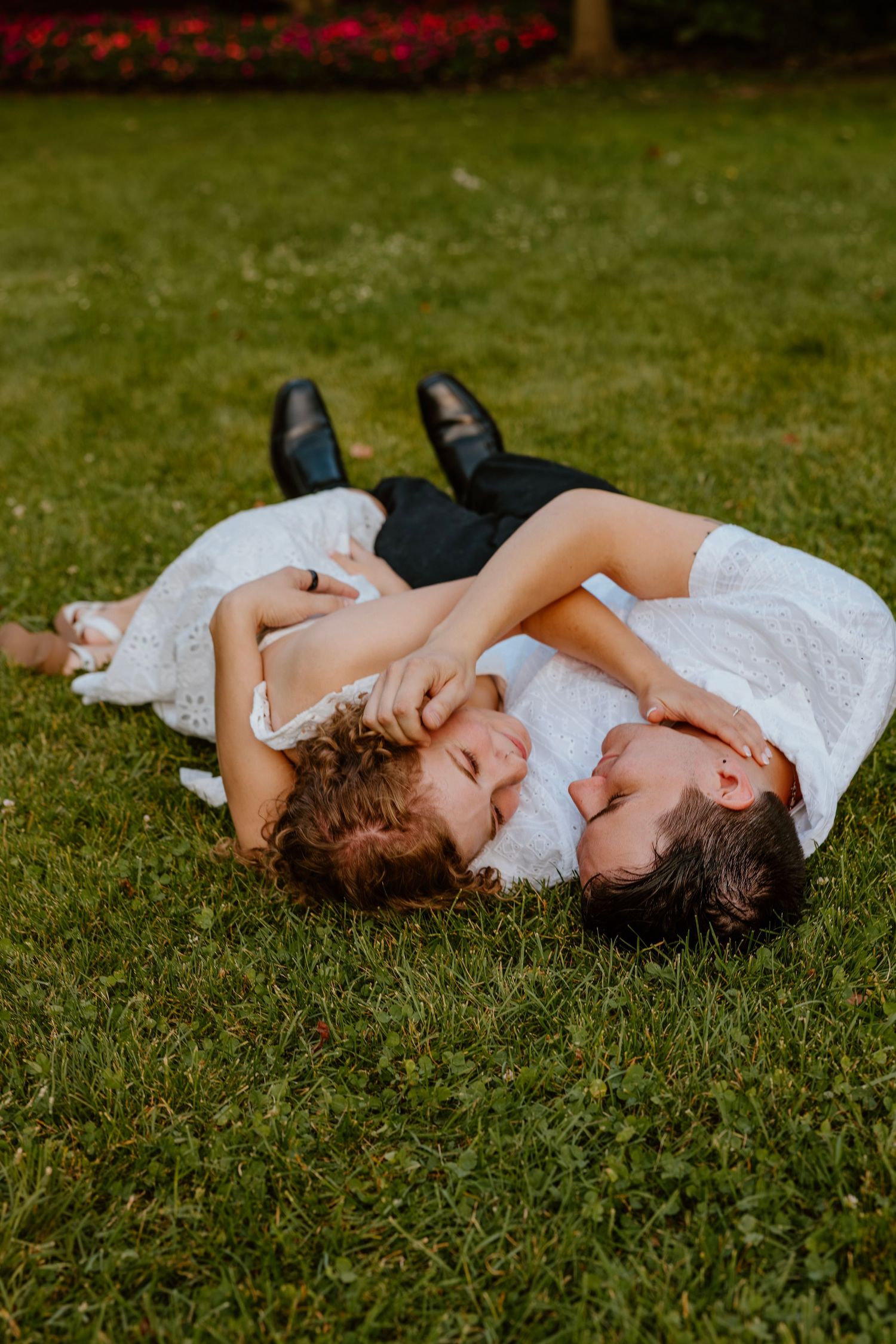 Bride and groom lying on lush green grass laughing together in wedding attire outdoors. Chicagoland engagement photos.