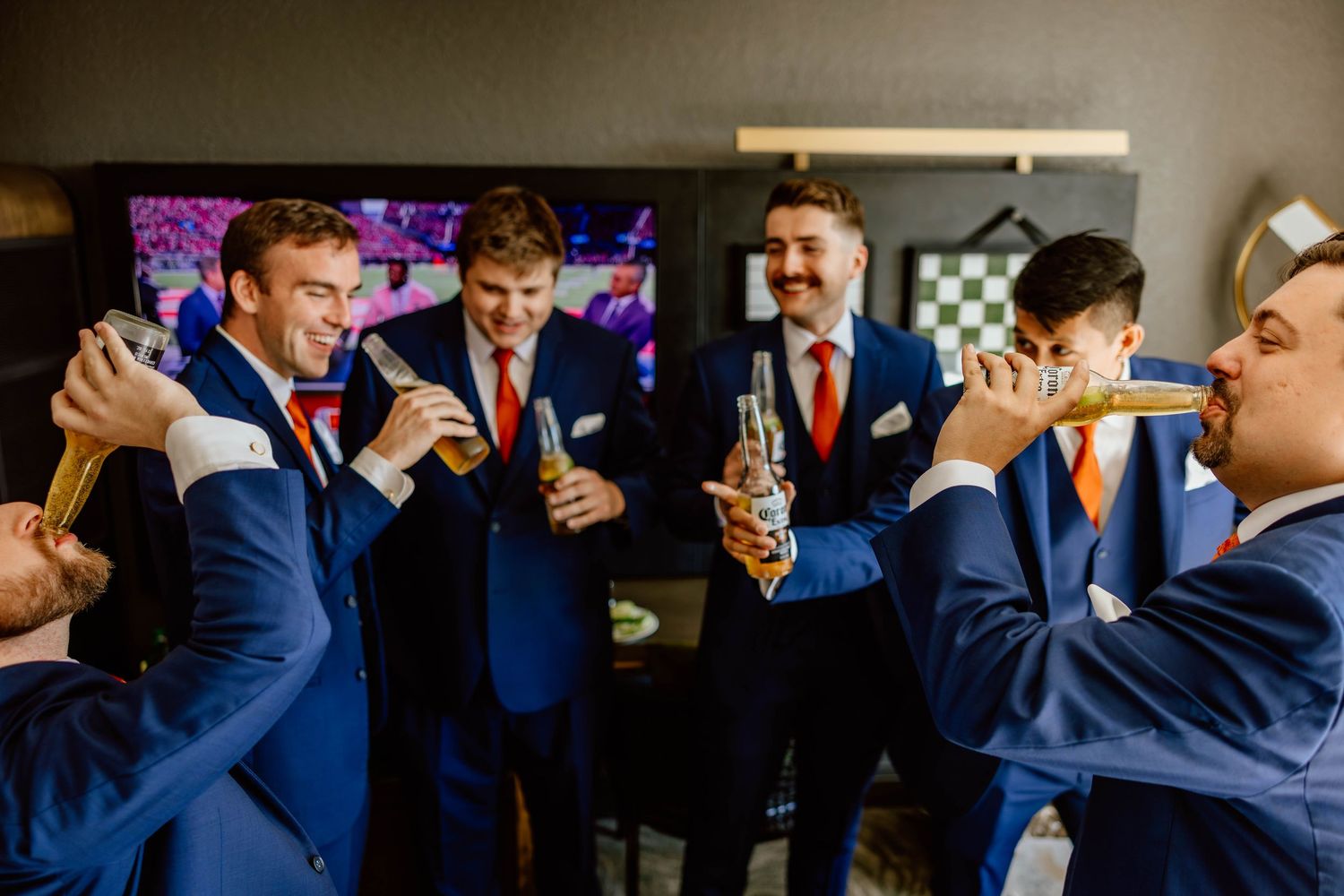 Groomsmen in navy suits with orange ties celebrating with drinks and cigars before wedding. Chicago hotel wedding photos.