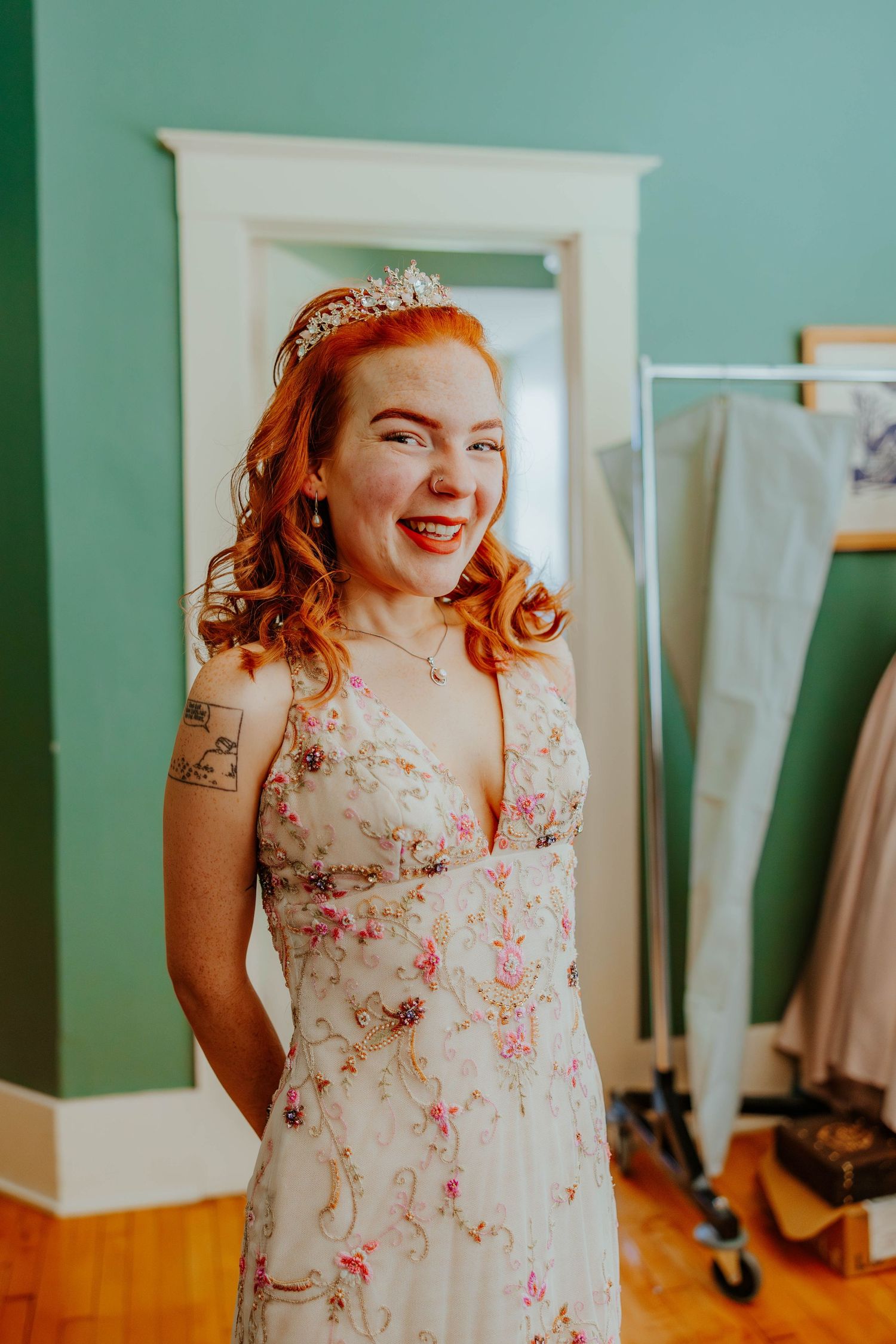Laughing red-haired bridesmaid wearing tiara and floral embroidered dress during wedding getting ready.