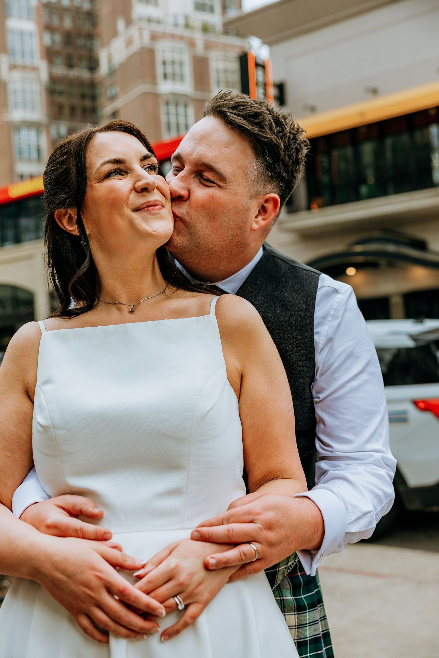 Groom in tartan kilt kisses bride on cheek outdoors in city. Chicago wedding reception Gibson's Bar and Steakhouse.