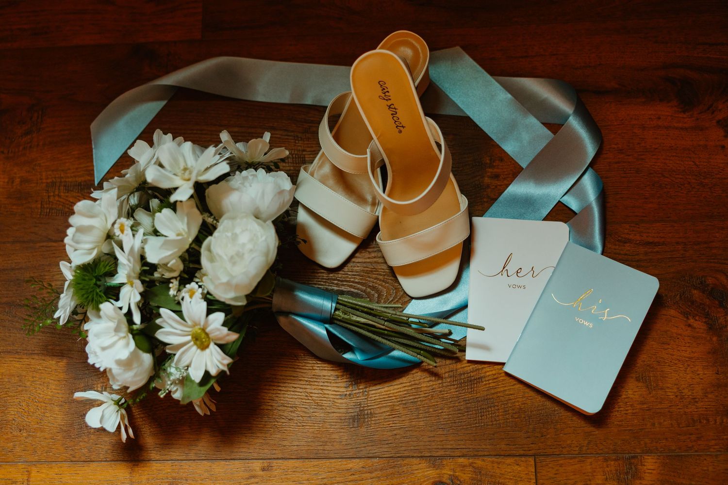 Wedding flat lay featuring white floral bouquet, gold heeled sandals, and teal vow books on wood. Michigan elopement.
