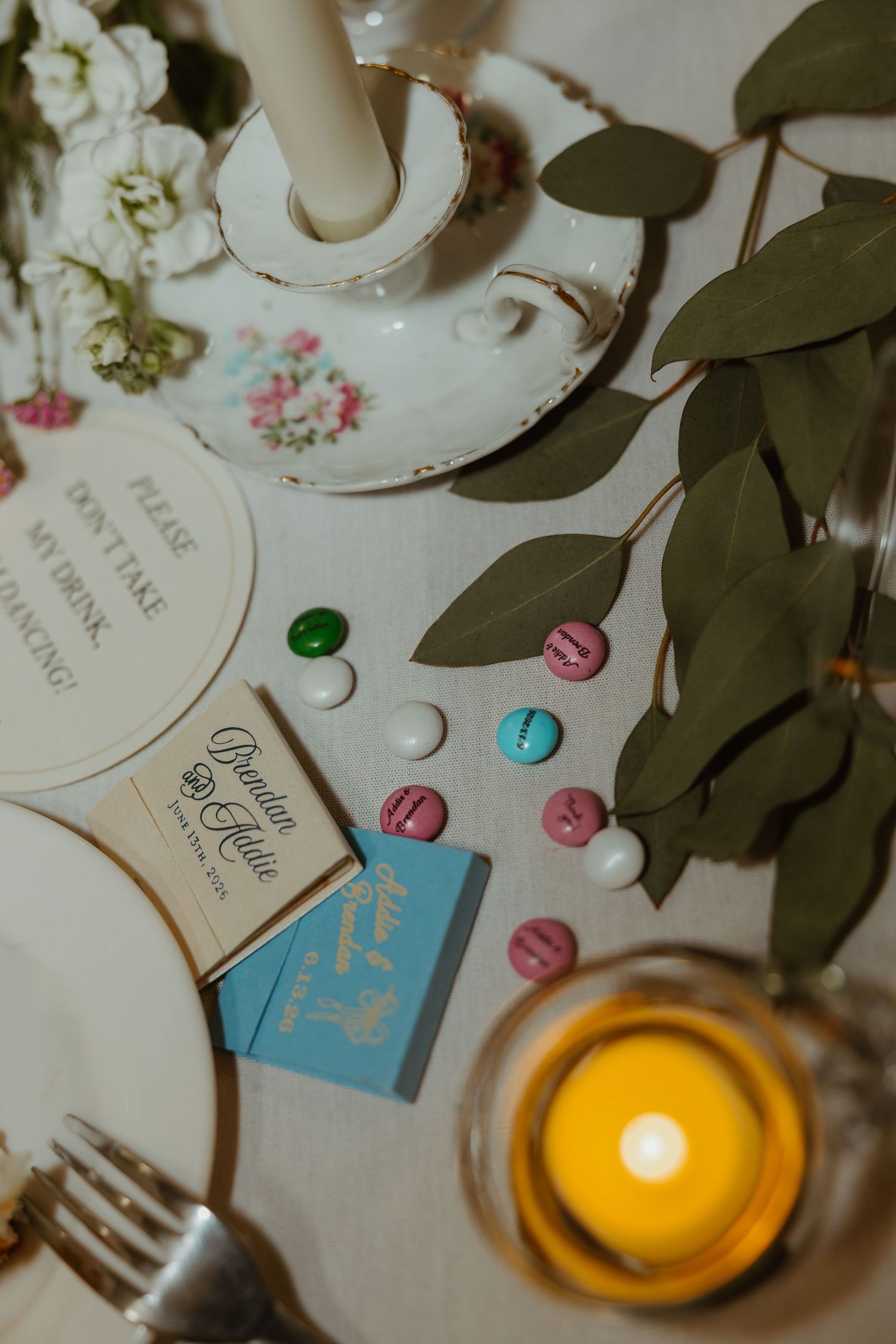 Wedding reception table detail with personalized matchbooks, colorful candies, candle, and floral decor.
