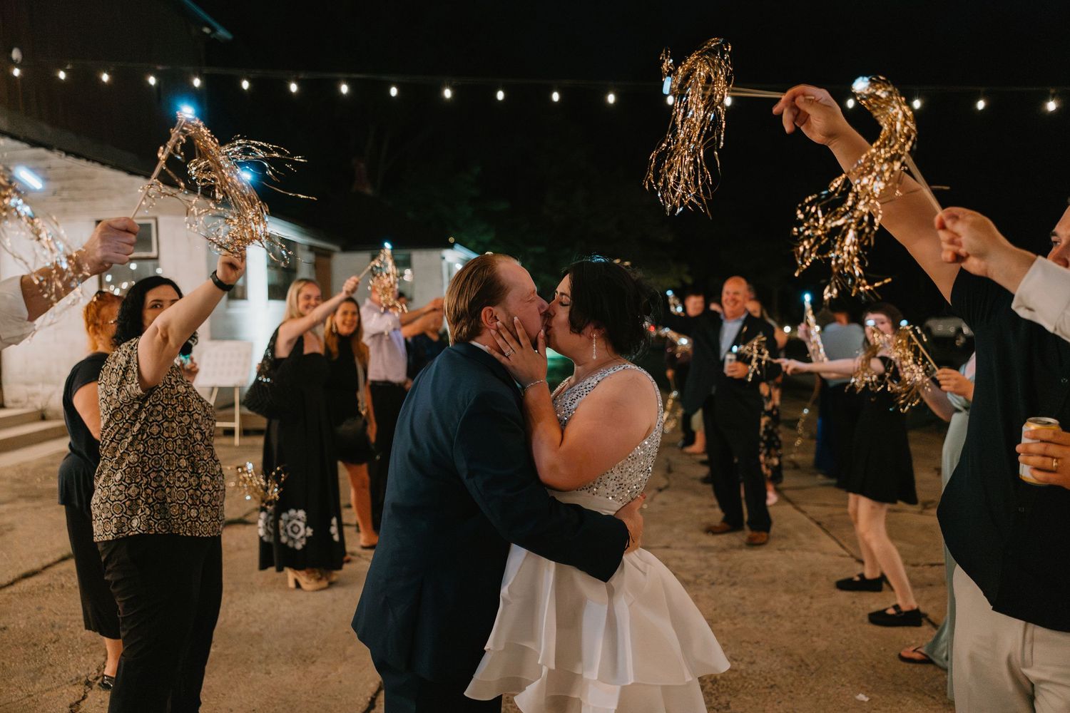 Bride and groom share romantic kiss surrounded by guests holding sparklers at night wedding sendoff. Northwest Indiana wedding venues.