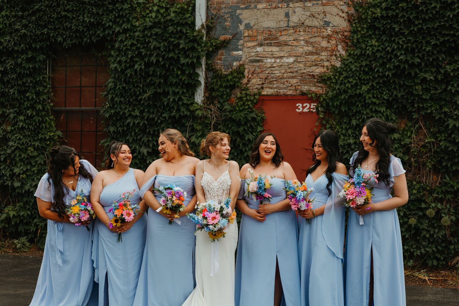 Bride in white lace gown with bridesmaids in blue dresses holding colorful bouquets. Chicagoland wedding venues.