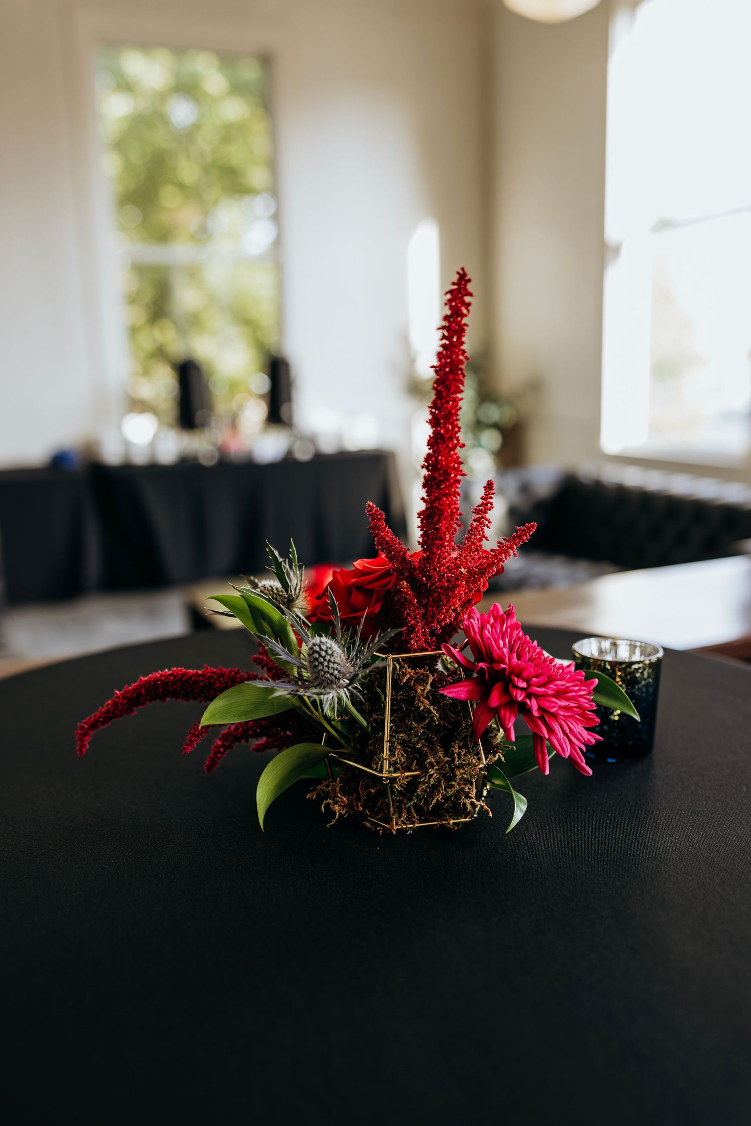 Bold red floral centerpiece with celosia and dahlias in a geometric vase on a black tablecloth. Crown Point Courthouse wedding.