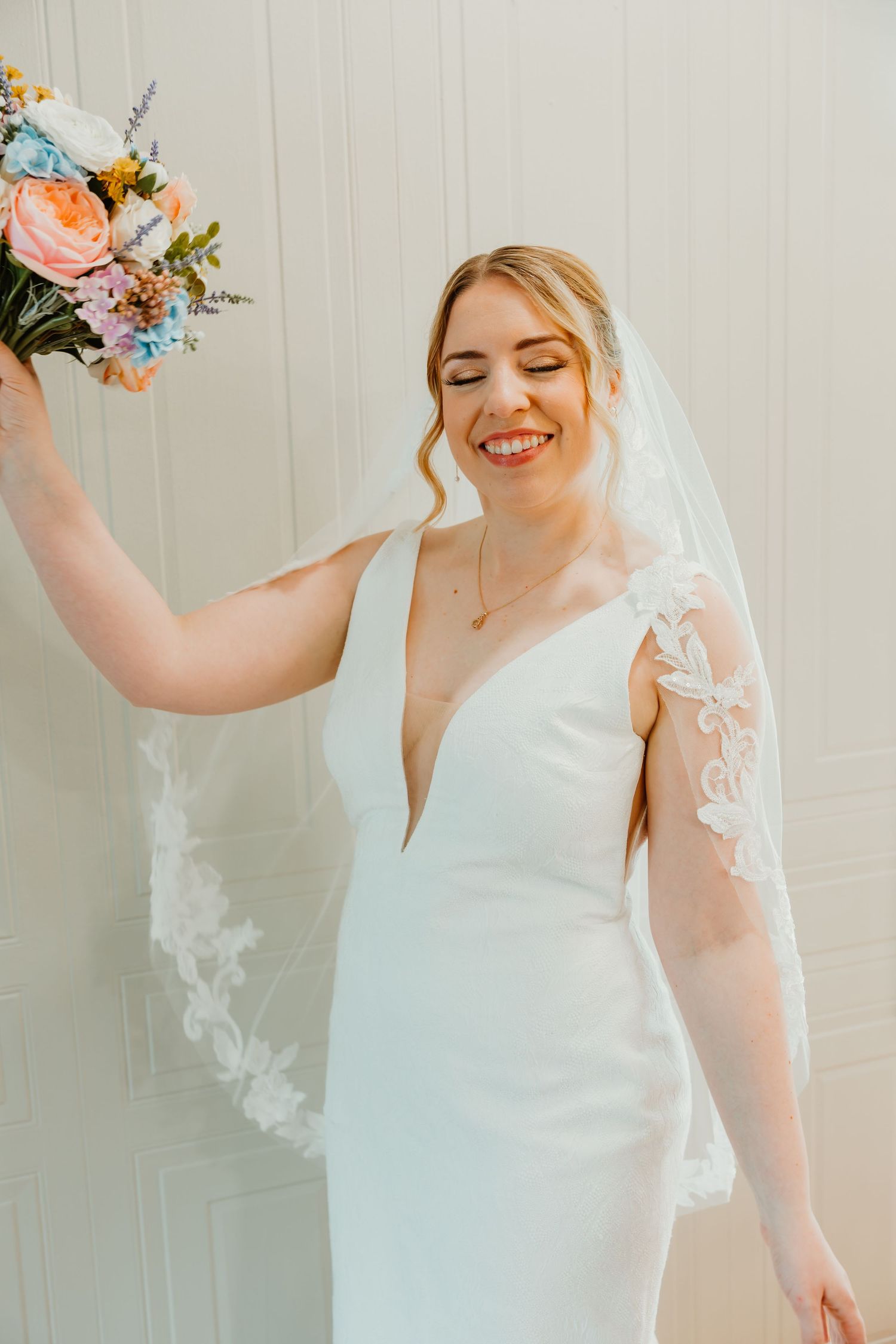 Radiant bride in a deep V-neck white wedding gown with lace veil holding a colorful pastel bouquet. Chicagoland wedding venues.