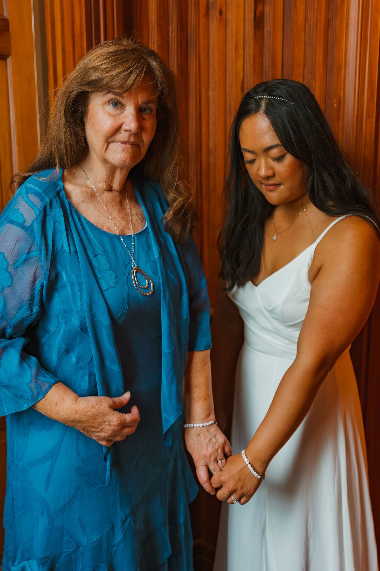 Older woman in teal dress holds hands with bride in white gown. Michigan elopement.
