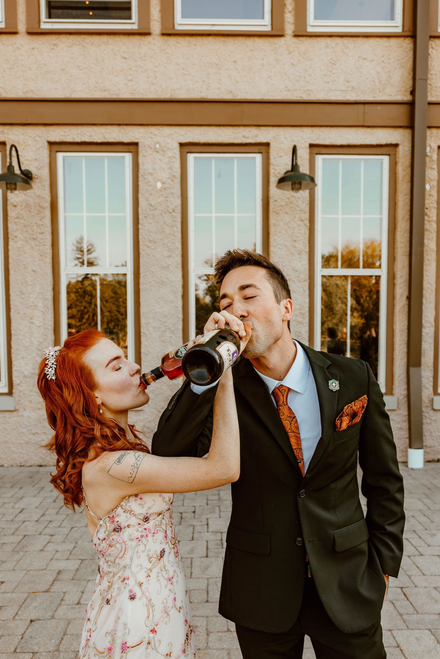 Bride and groom sharing a champagne bottle toast outside a wedding venue.