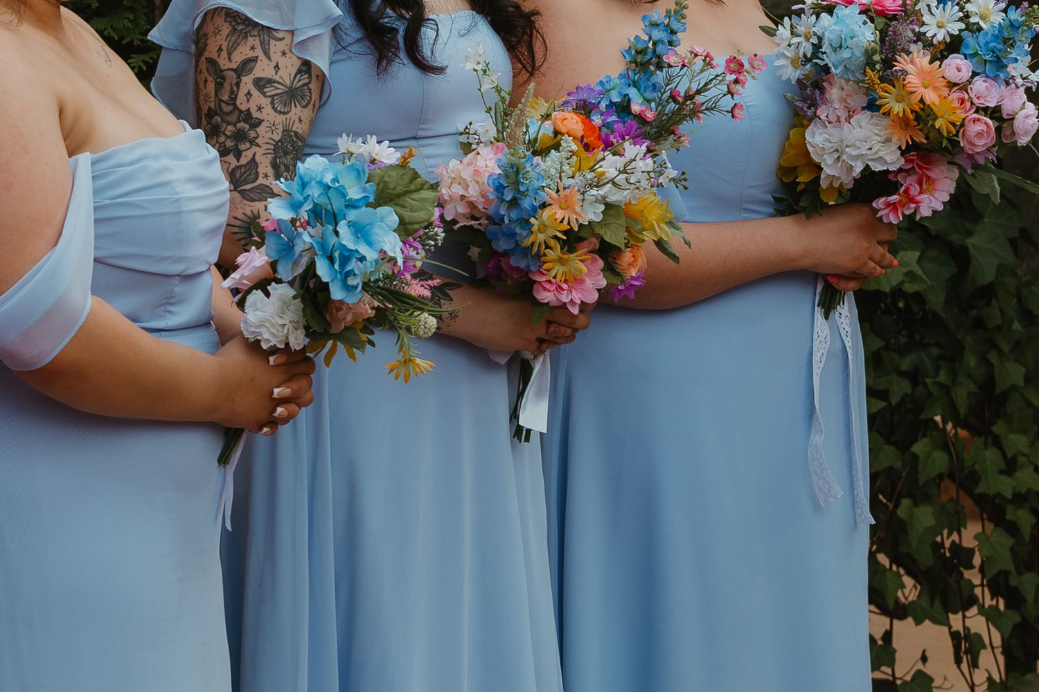 Bridesmaids in powder blue dresses holding vibrant multicolored wildflower bouquets at outdoor wedding ceremony. Chicagoland wedding venues.