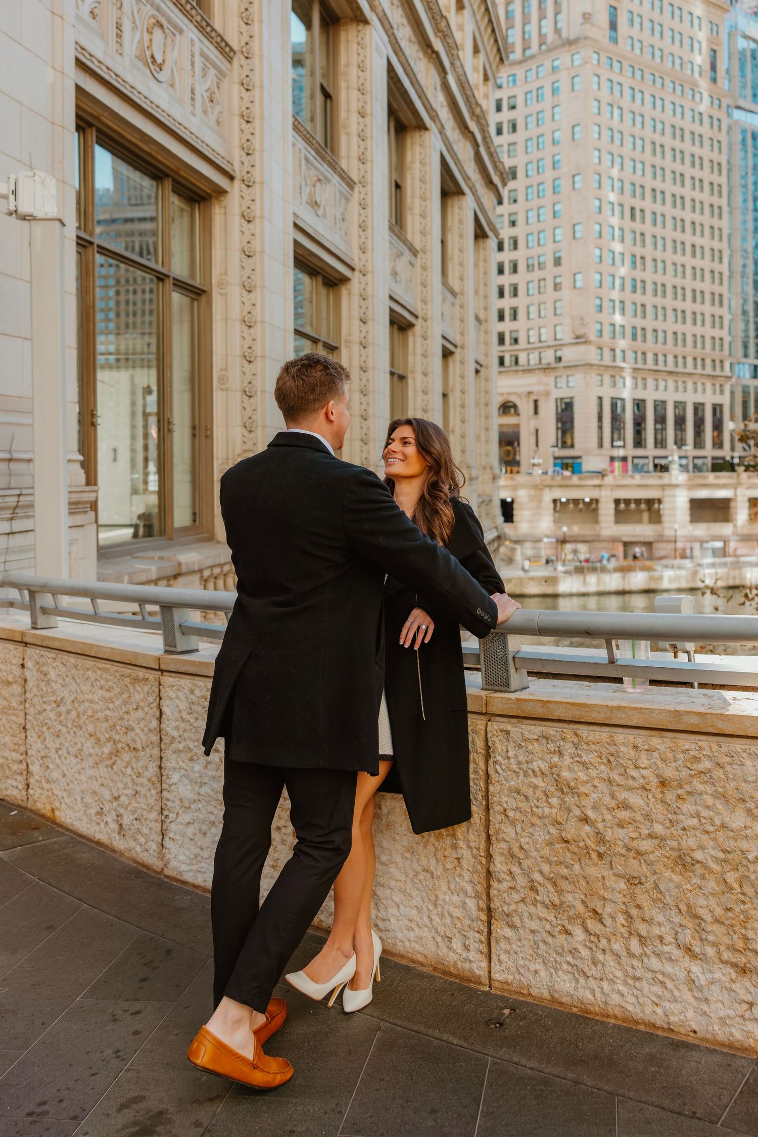 Couple sharing a romantic moment on an urban terrace overlooking a city river and skyline. Outdoor Chicago engagement photos.