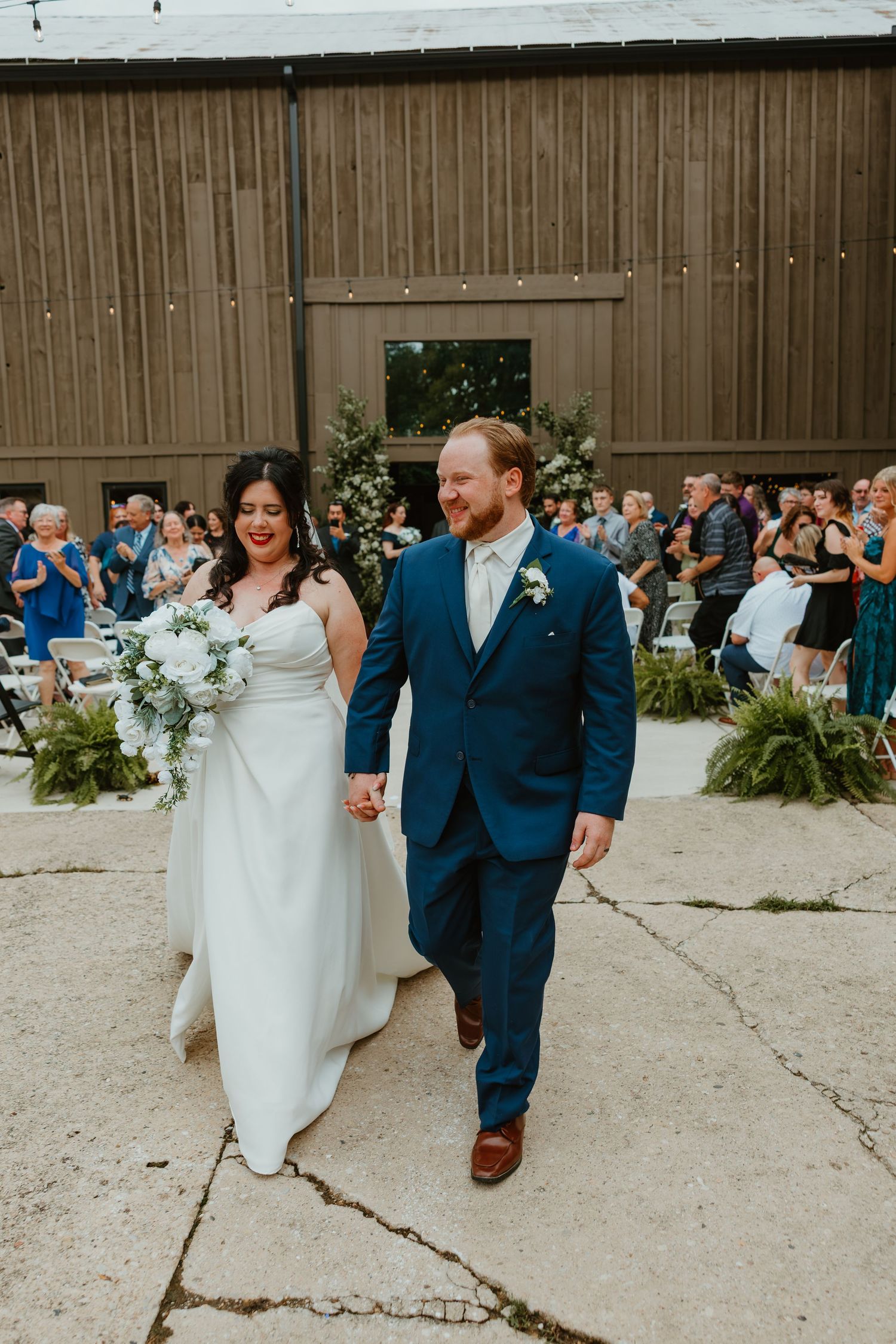 Newlywed couple walks hand in hand down the aisle after their outdoor barn wedding ceremony with guests applauding. Northwest Indiana venues