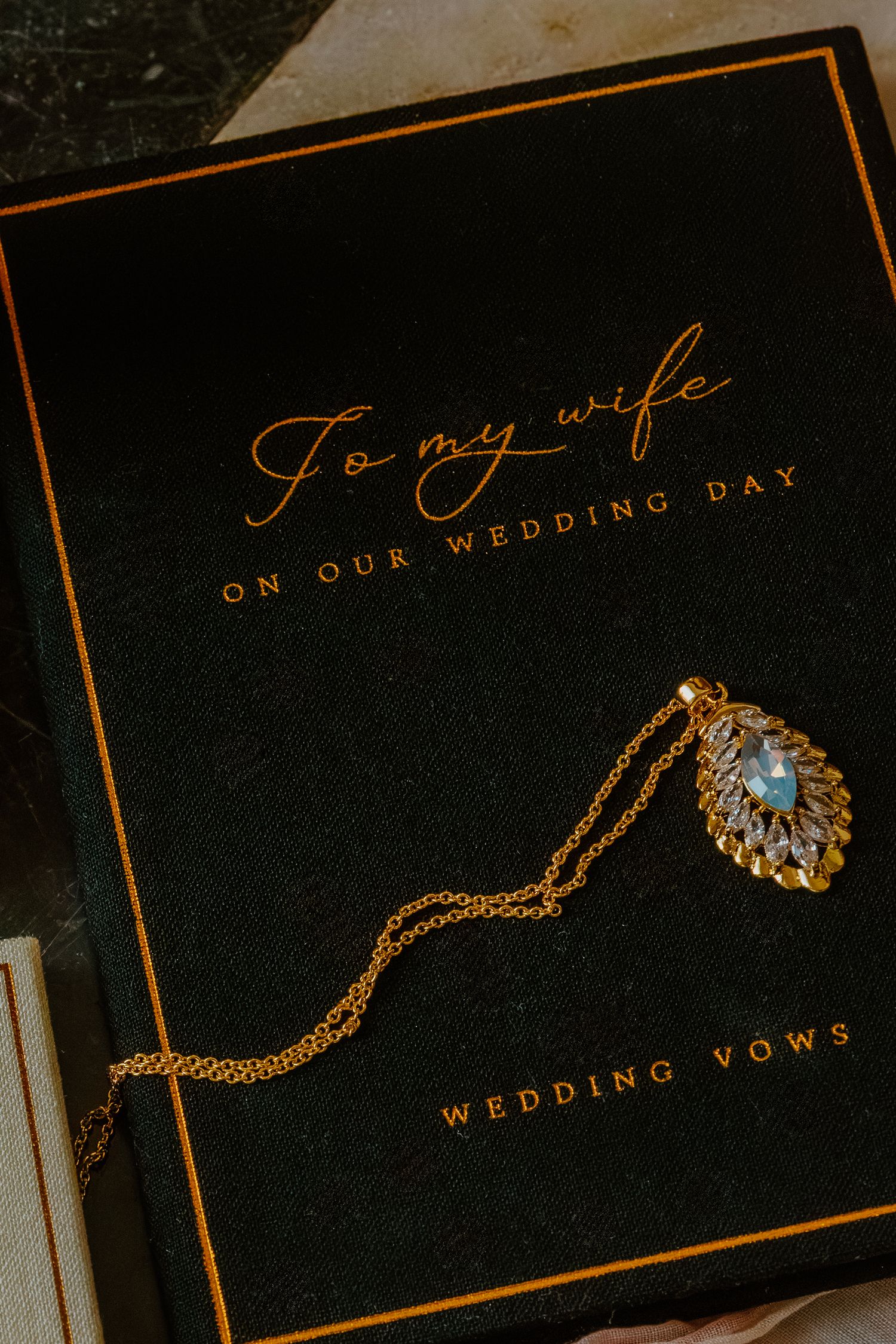 Gold necklace with teardrop pendant resting on a black wedding vows book inscribed To My Wife. Crown Point Courthouse wedding.